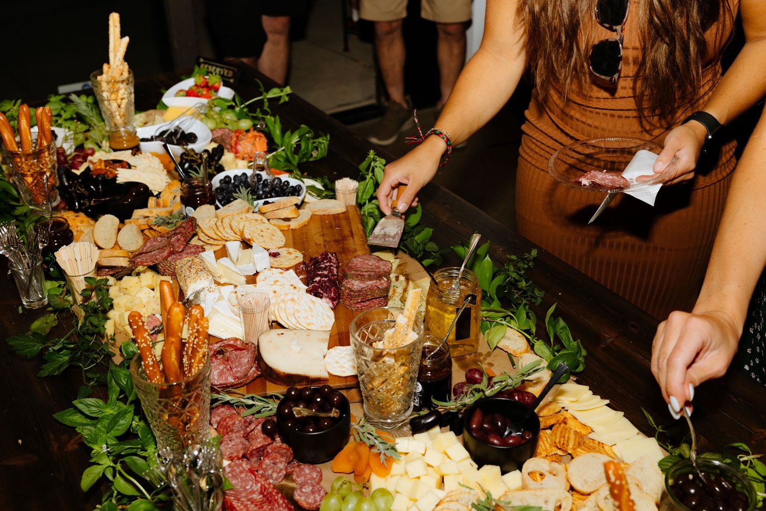 Catering table with assorted charcuterie, cheeses, fruits, and decorative greenery displayed at an elegant event.