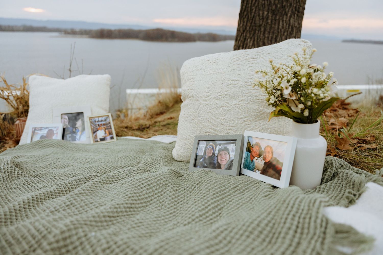A row of framed photographs displayed on a textured blanket outdoors with a lake view in the background.