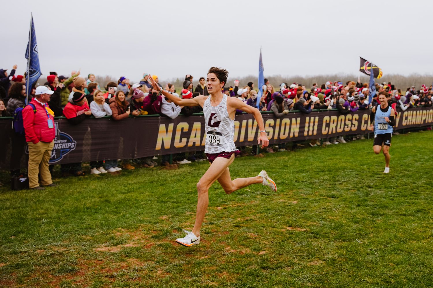 Athletes compete in a cross country race on a grassy course with spectators lining the path.