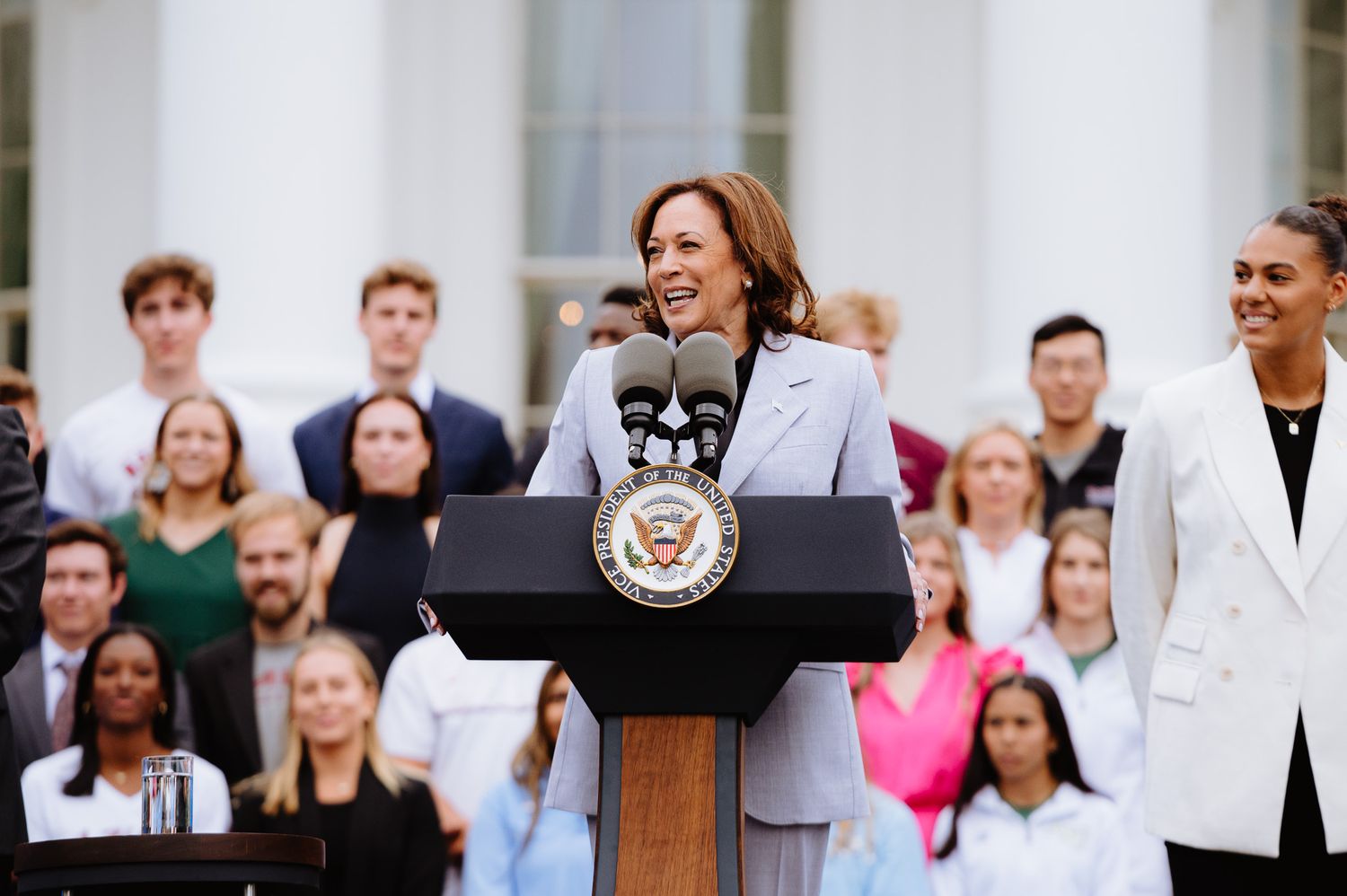 Group of people gathered at a formal event with American flags visible in background.
