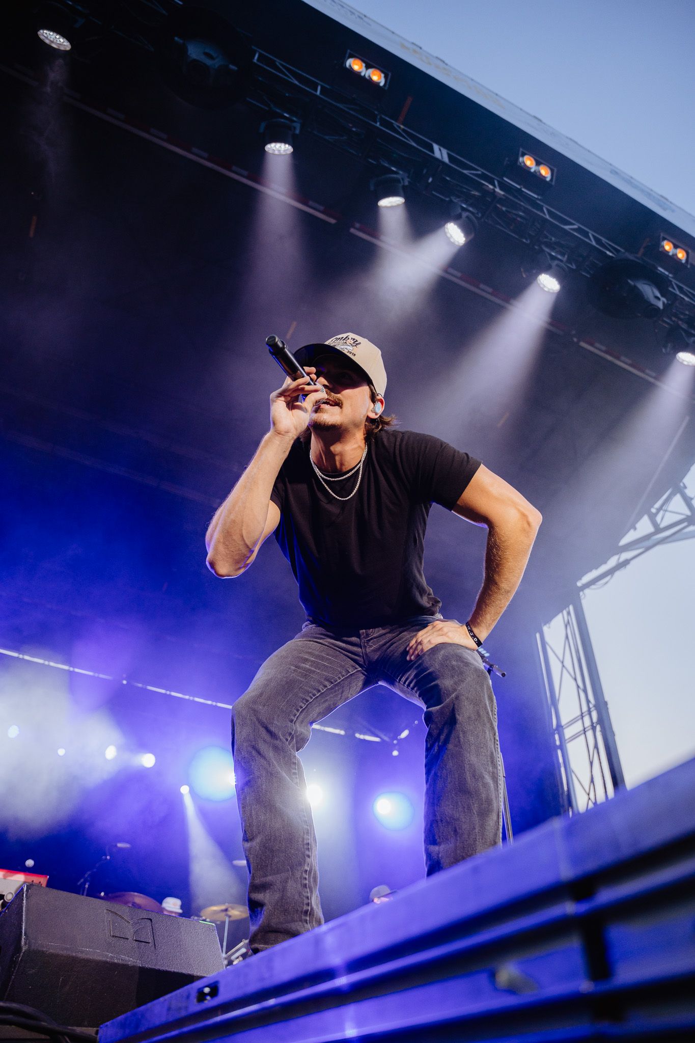 Dynamic stage performance with performer in casual attire against blue and purple concert lighting.