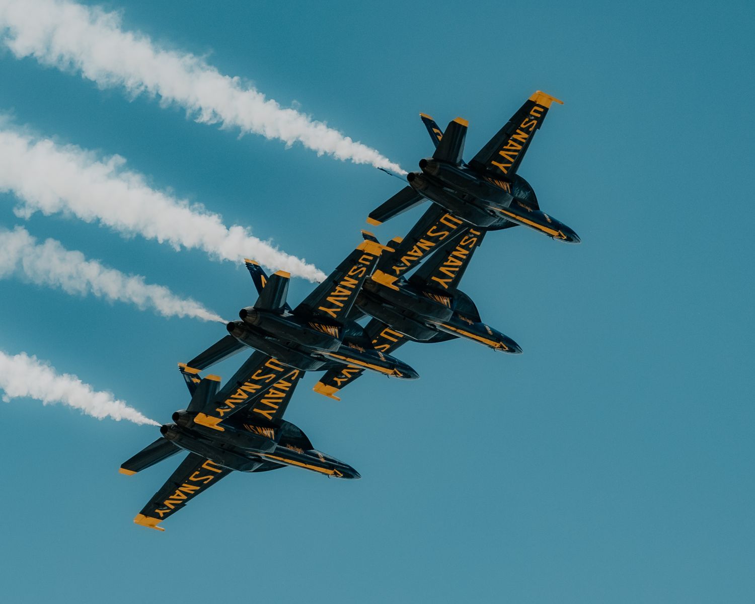 Stunt plane performs aerial maneuver leaving white smoke trails against bright blue sky.