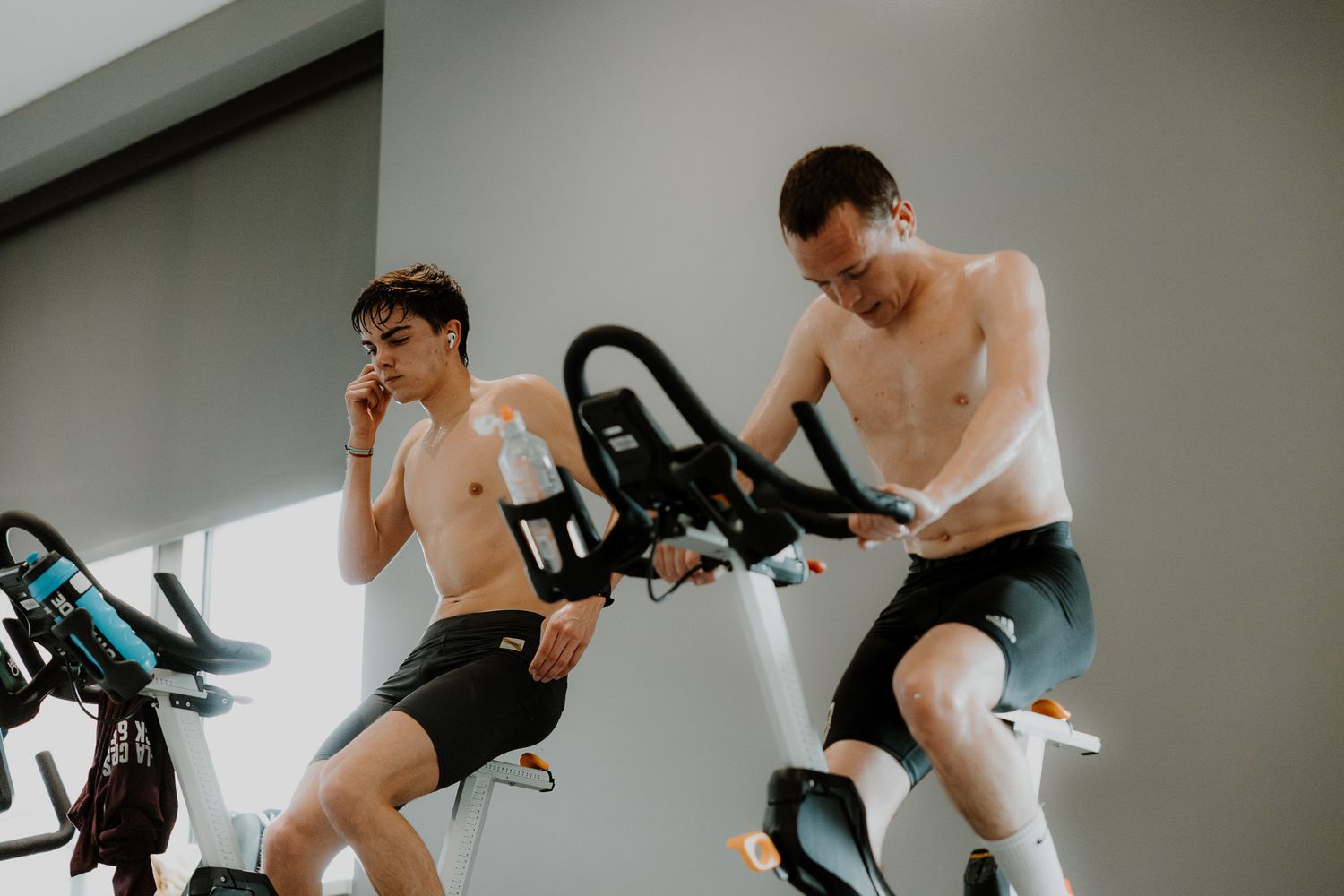 Athletes exercising on stationary bikes in a bright indoor fitness studio during an intense workout session.