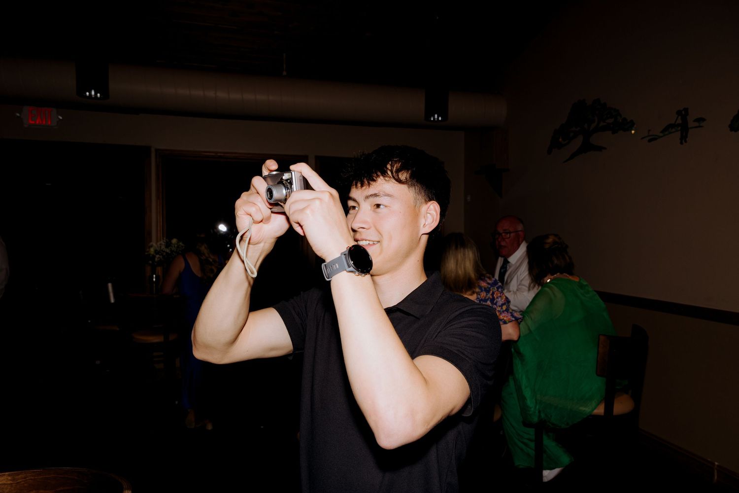 Person takes a photo using a camera in a dimly lit indoor setting.