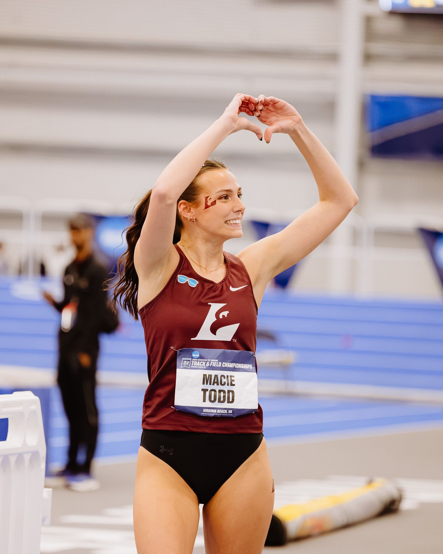 Athletes in maroon uniforms performing stretches in an indoor track facility.