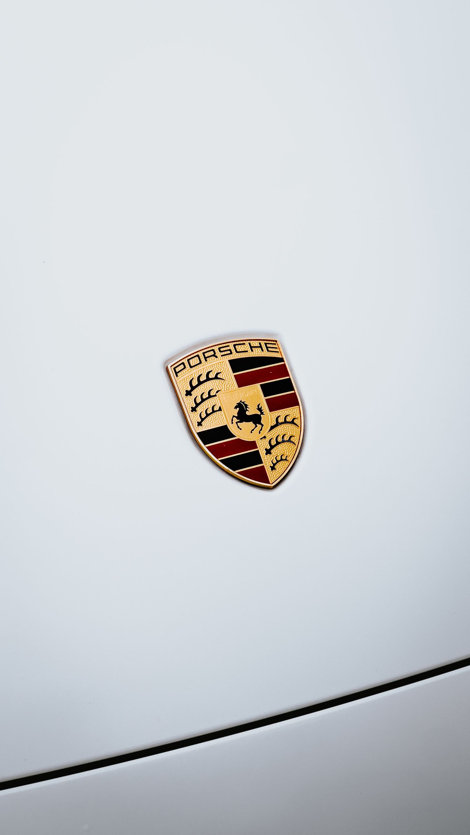 Close-up view of multiple Porsche emblems on a light background showing the iconic gold and black shield design.