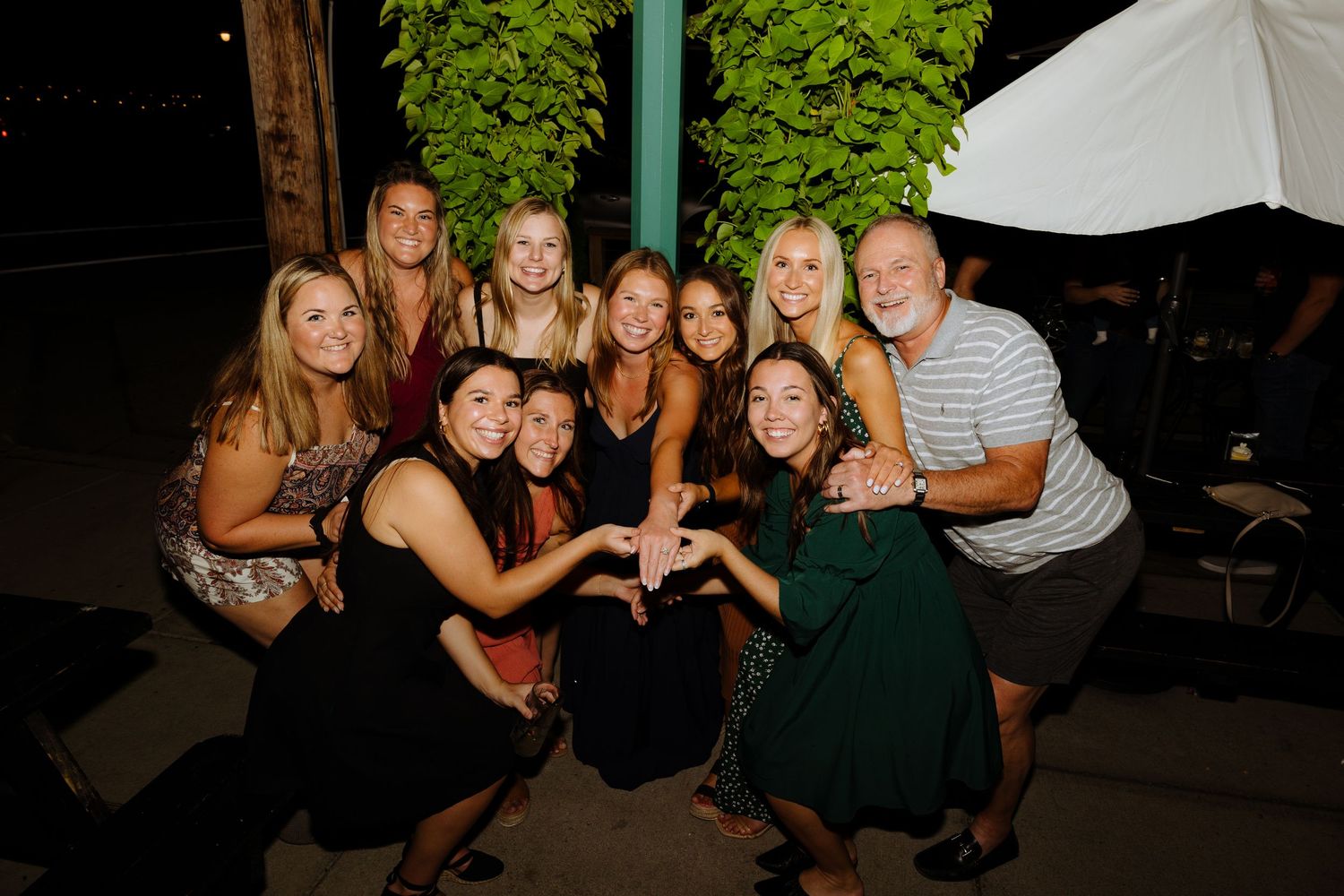 A group of friends pose together making heart shapes with their hands at an outdoor nighttime gathering.