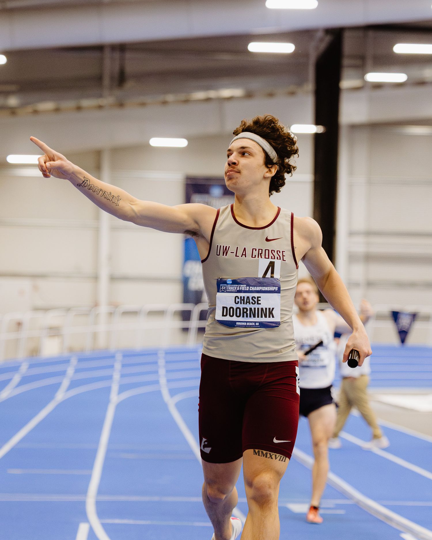 Track athletes competing in an indoor race leaning forward at the finish line.