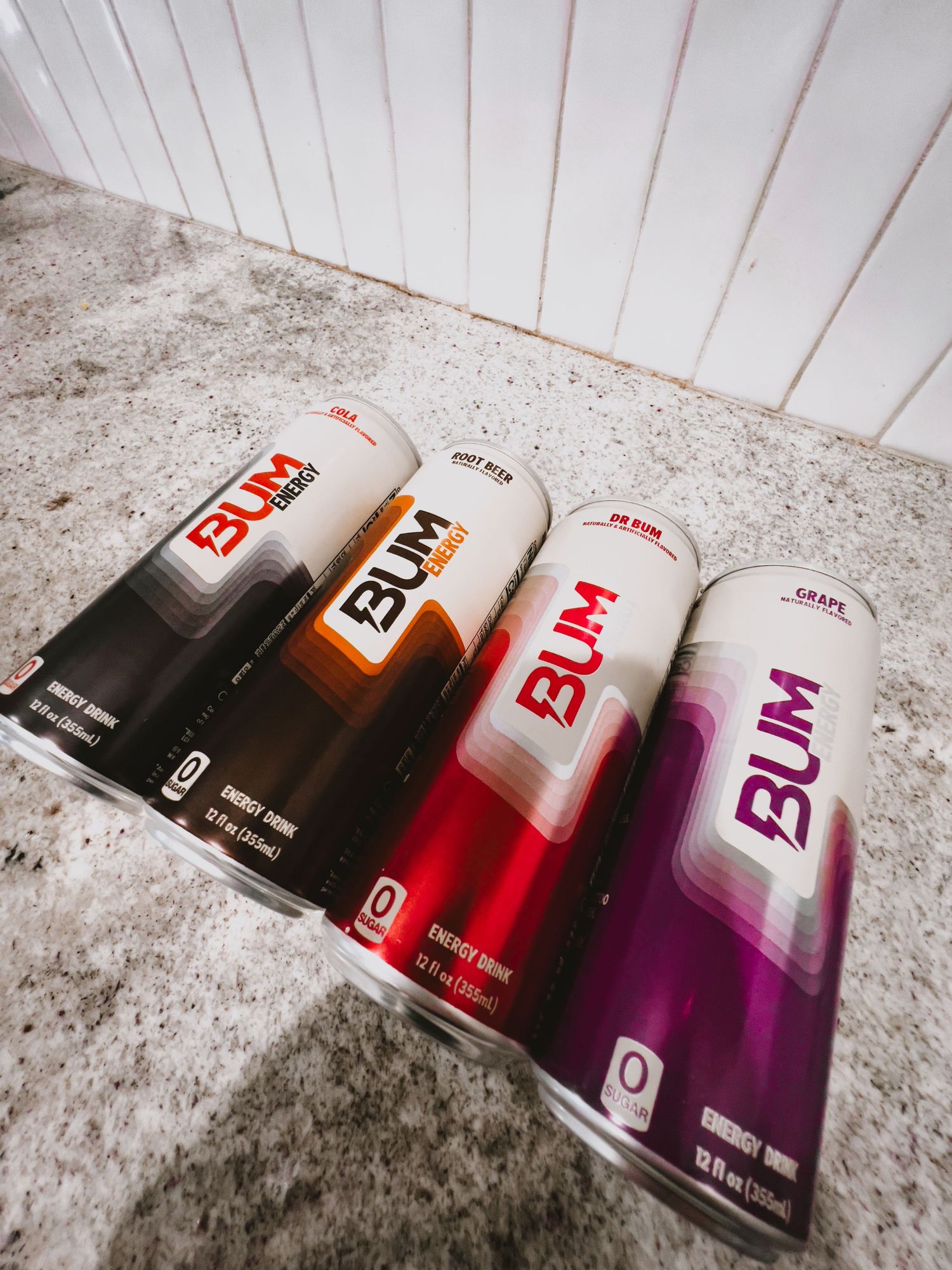 Energy drink cans arranged in a gradient from black to red to purple creating an artistic composition on concrete surface.