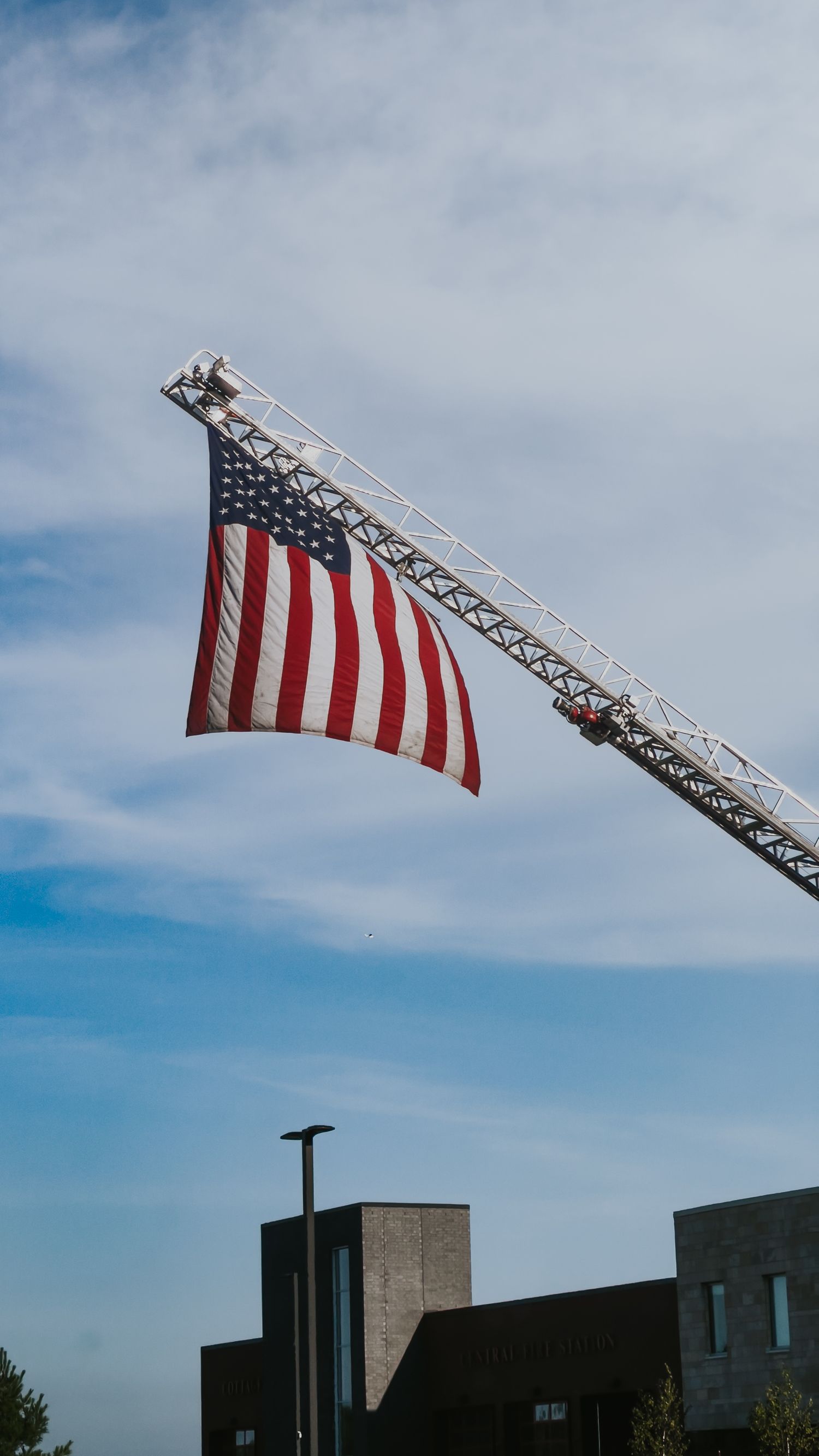 An American flag hangs from a construction crane against a blue sky with modern buildings below.