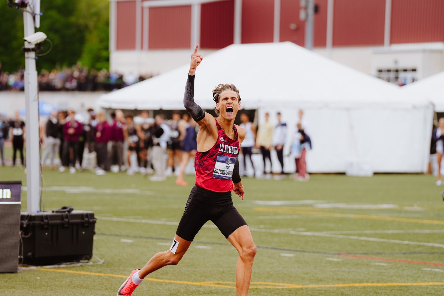 Athletes compete on a grass field during a track and field competition with a red barn in the background.