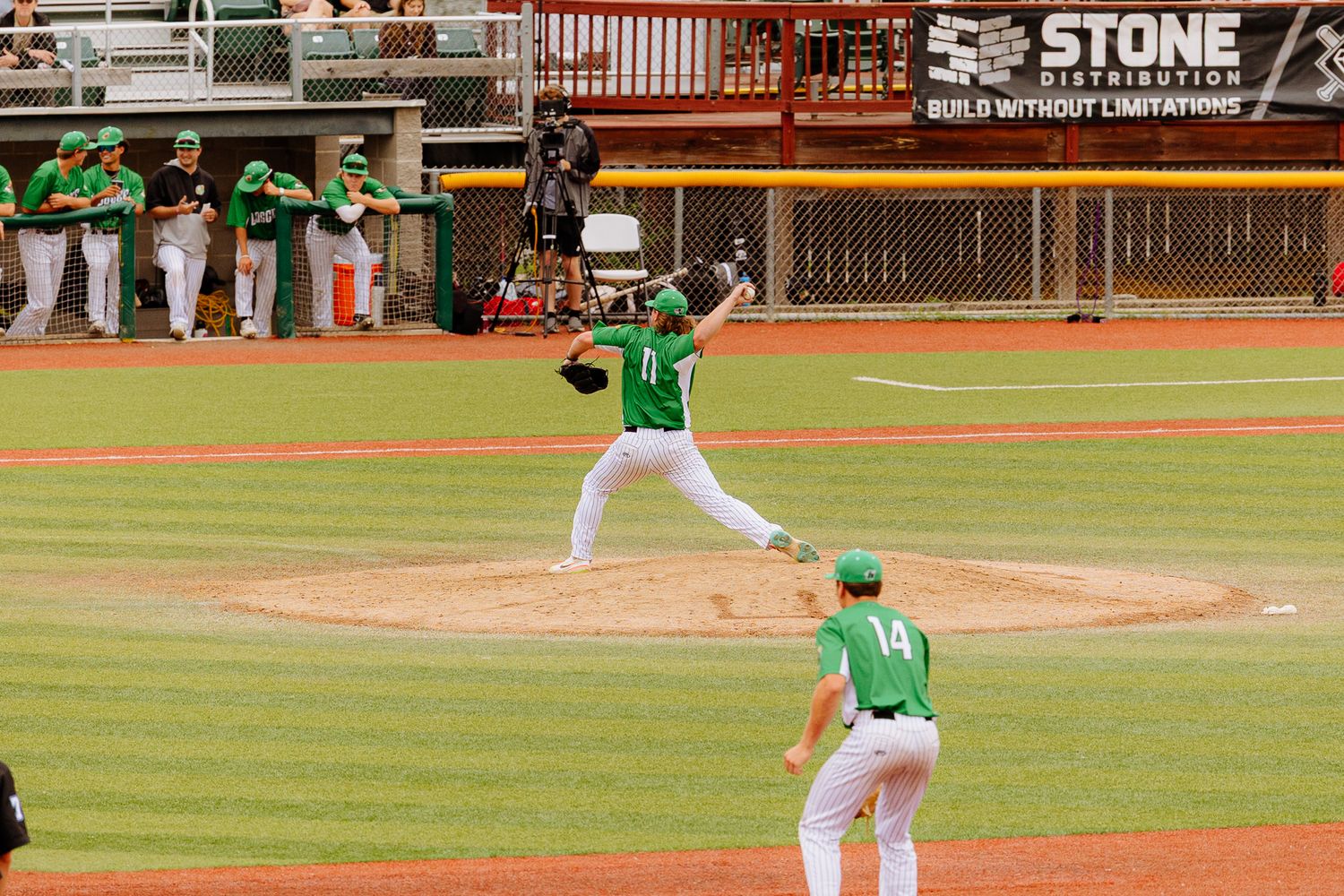 Baseball players in action on a sunny day at a field with advertising banners visible.