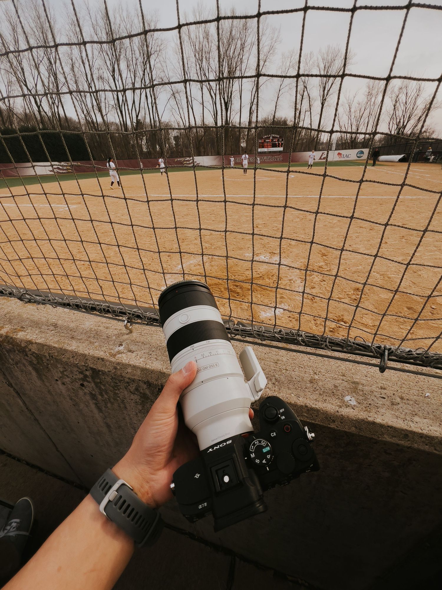 A sequence of photos showing a camera lens being aimed through a wire fence at a baseball field.