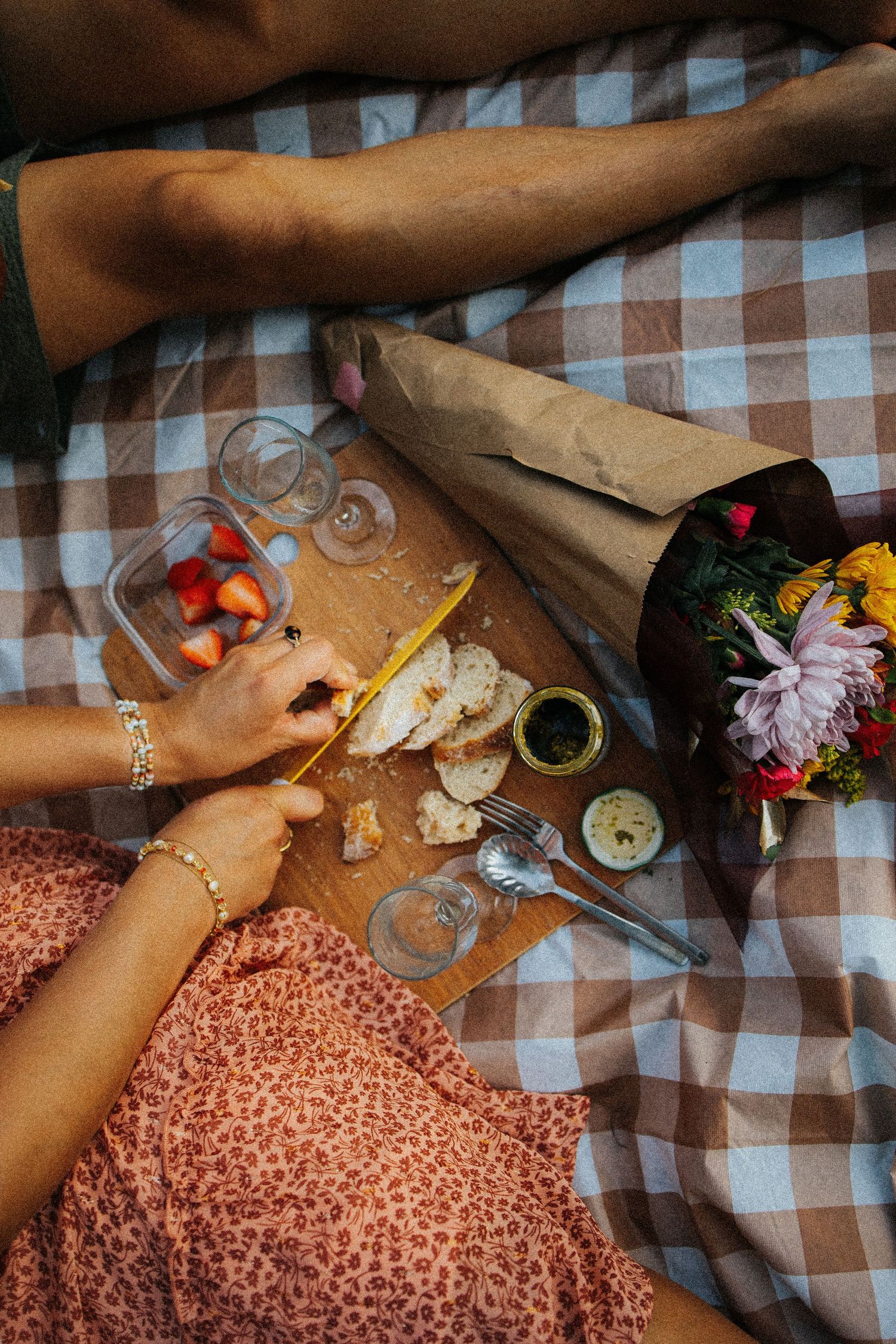 Hands creating art on a checkered tablecloth with flowers, pencils, and art supplies scattered around.