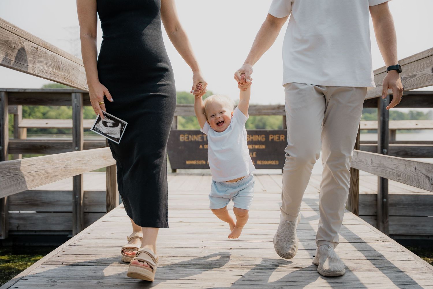 People in light and dark clothing walking together on a wooden boardwalk or deck in a casual outdoor setting.