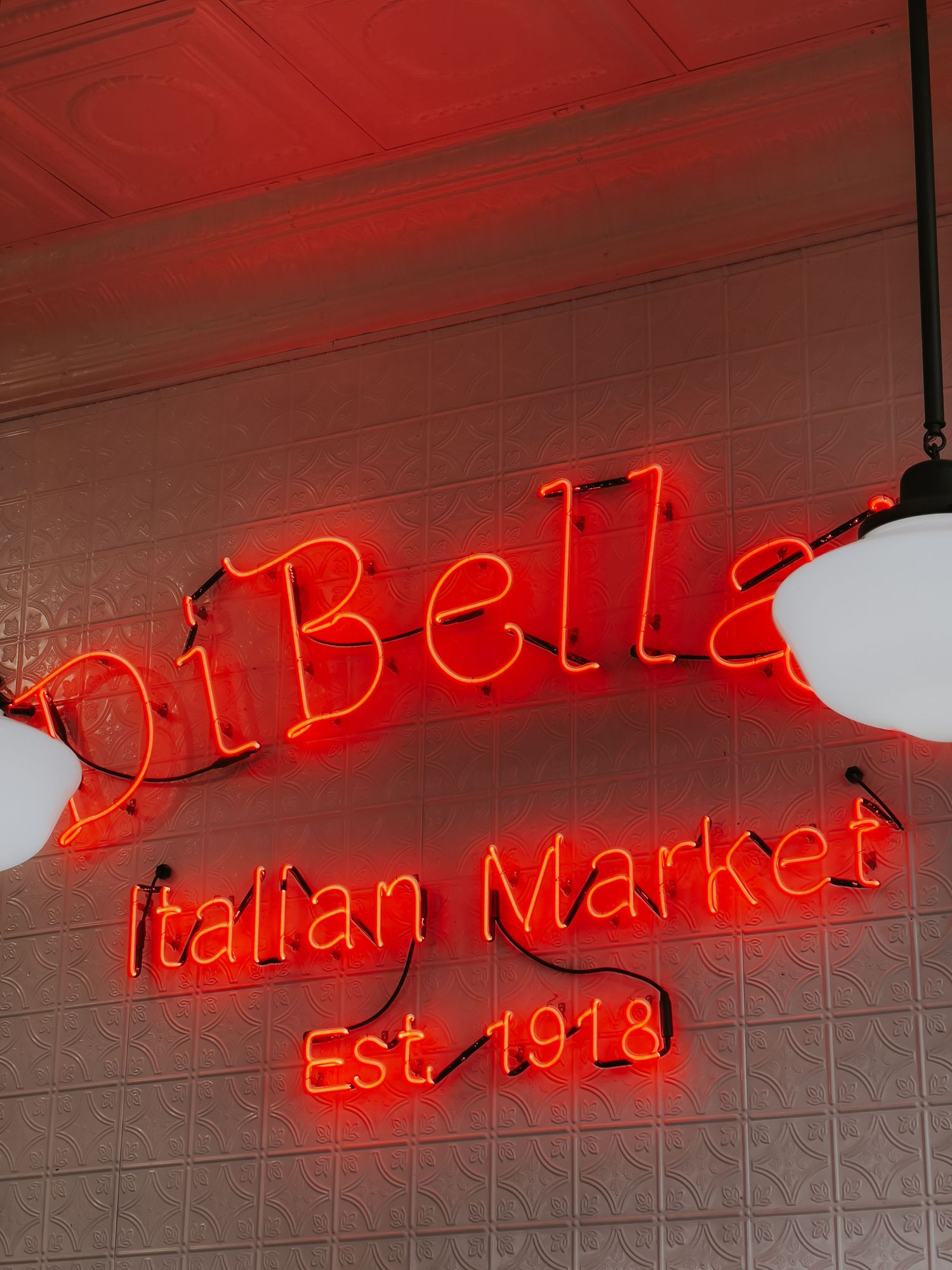 Glowing red neon sign for DiBella's Italian Market established in 1918 mounted on a gray wall.
