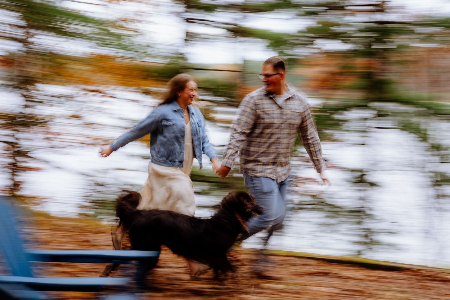 Motion blur photo of couple holding hands running with their black dog in an outdoor setting.