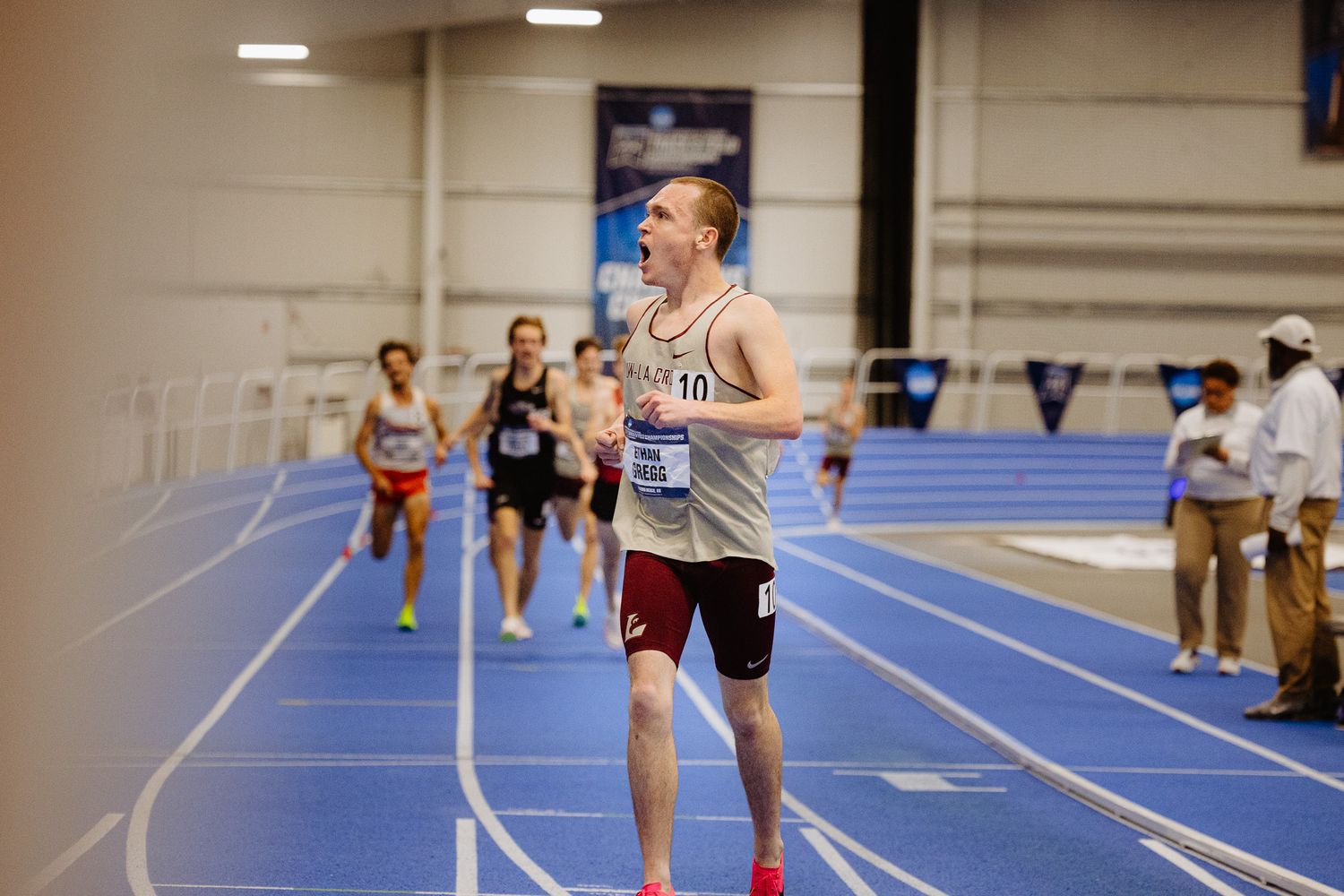 Indoor track athletes racing on a blue running track during a competition event.