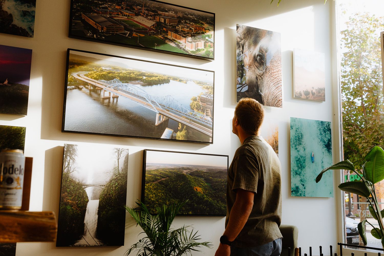 Art gallery interior showing framed photographs and paintings displayed on white walls with natural lighting.