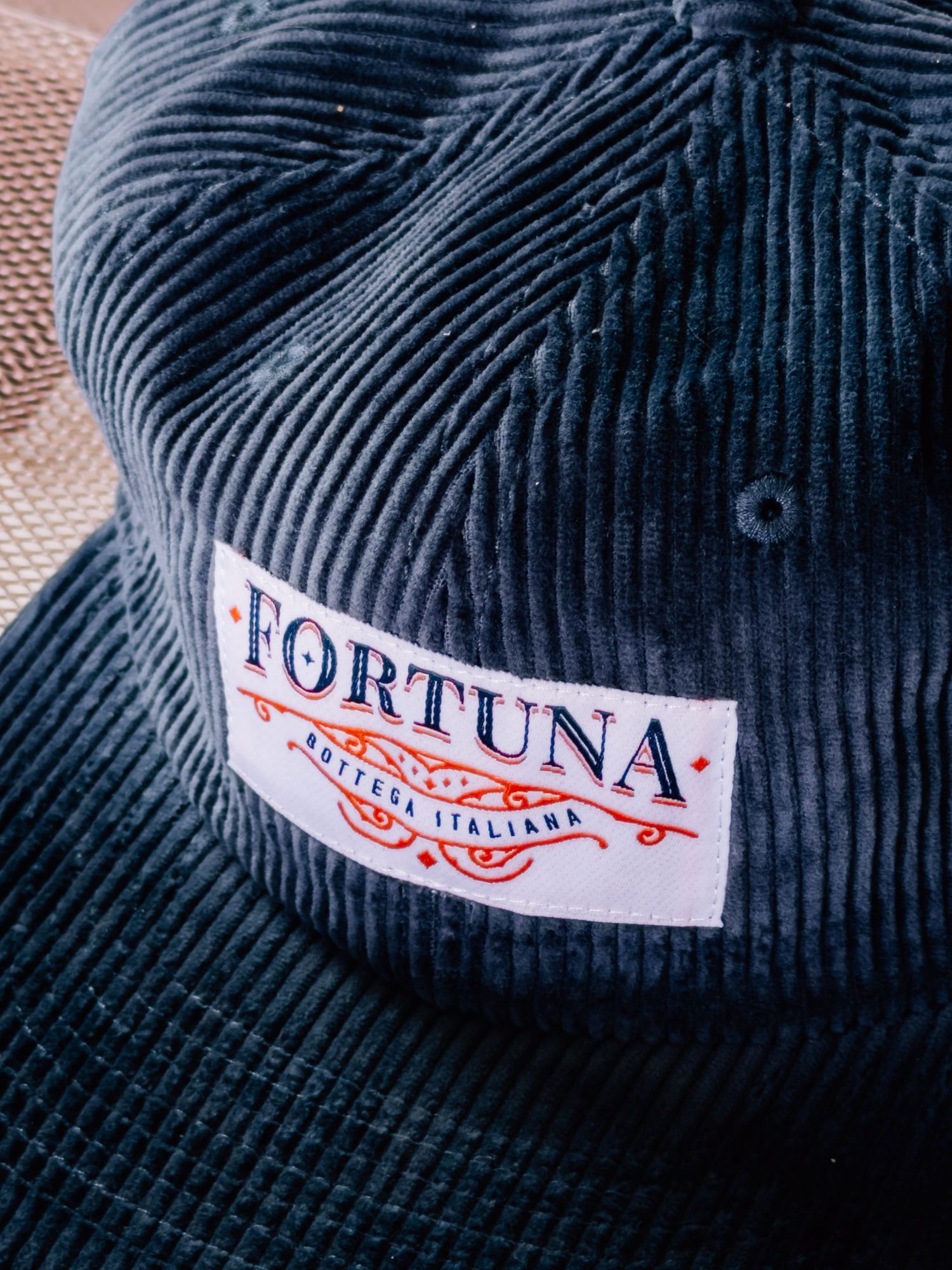 Close-up of a navy blue corduroy baseball cap with a white Fortuna brand patch on the front.