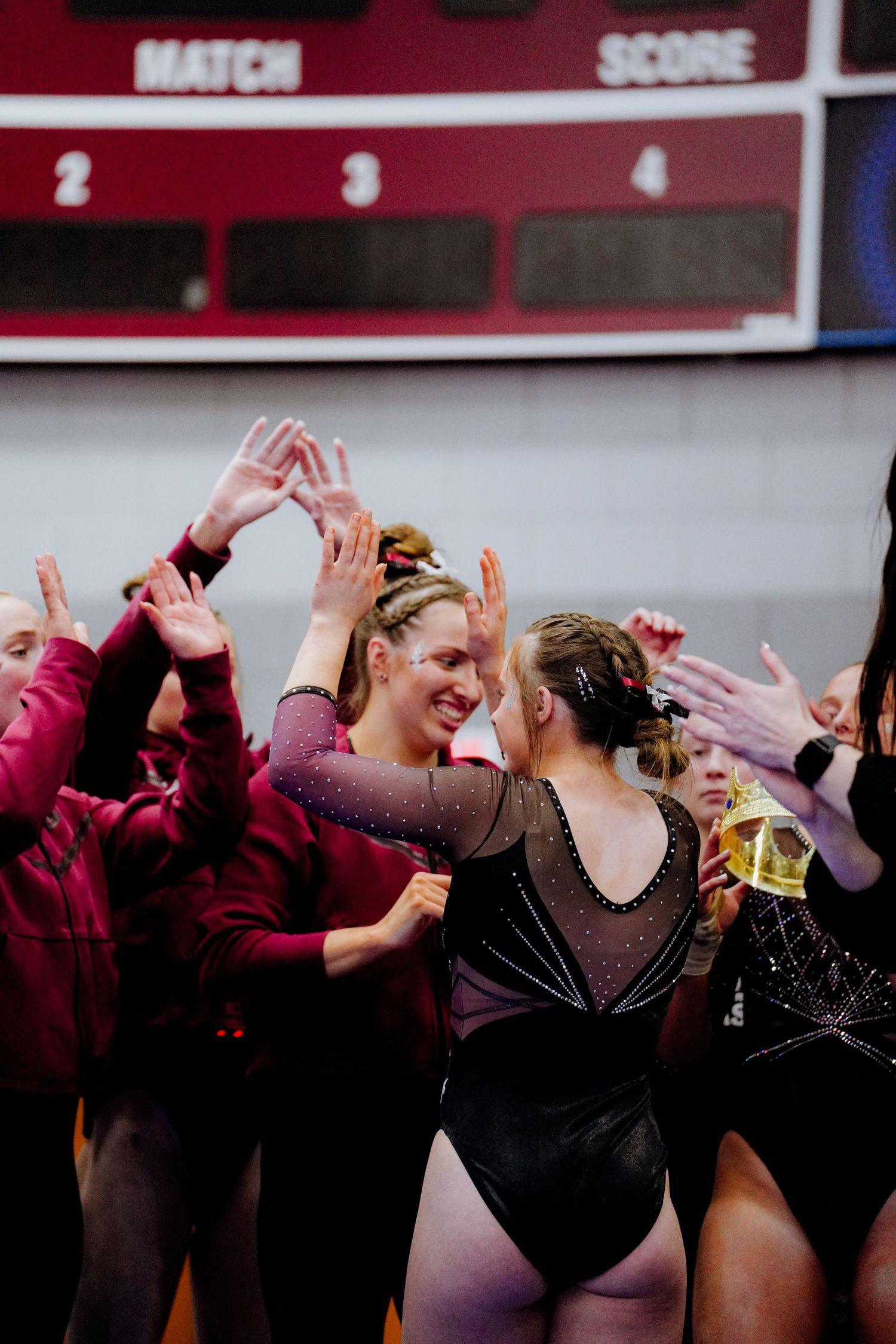 Gymnasts in black leotards celebrate together with high fives and cheers during a competition event.
