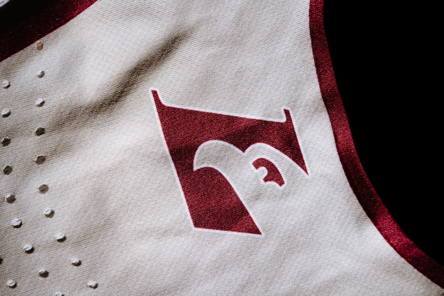 Close-up detail of a white sports jersey with a red F logo embroidered on the fabric.
