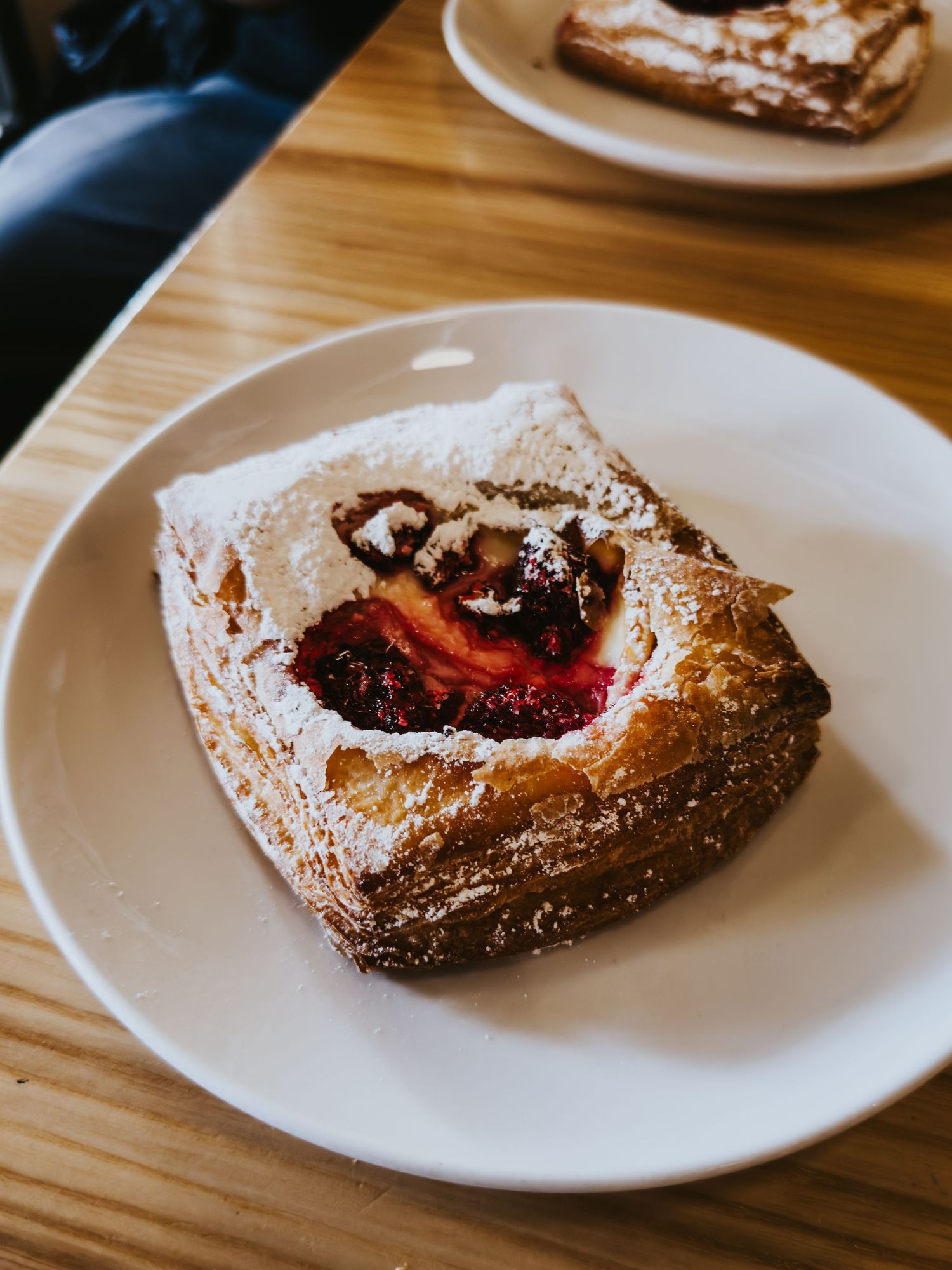 Freshly baked pastries with berry filling and powdered sugar on white plates arranged on a wooden table surface.