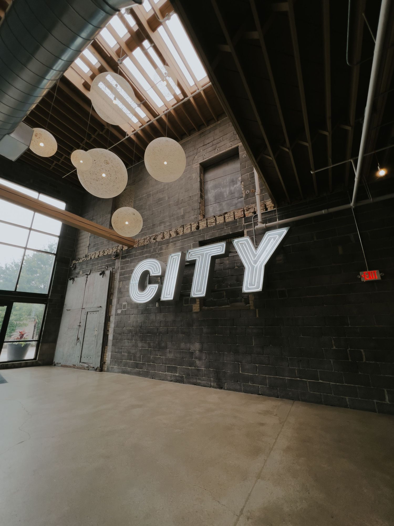 Modern industrial loft space with exposed brick walls, high ceilings, and white CITY lettering mounted on dark walls.