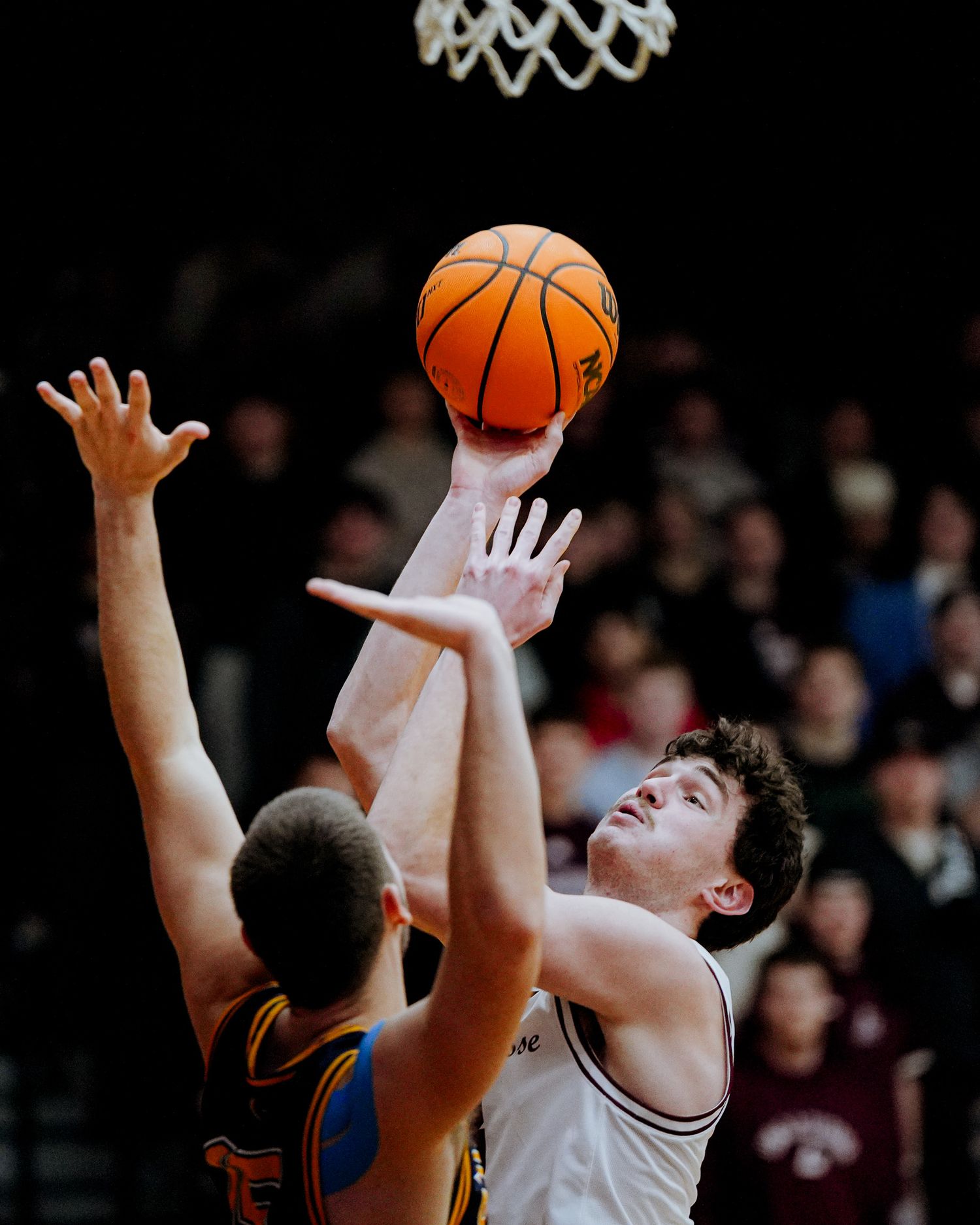 Basketball players leap high to grab a rebound under the hoop during an intense game action moment.