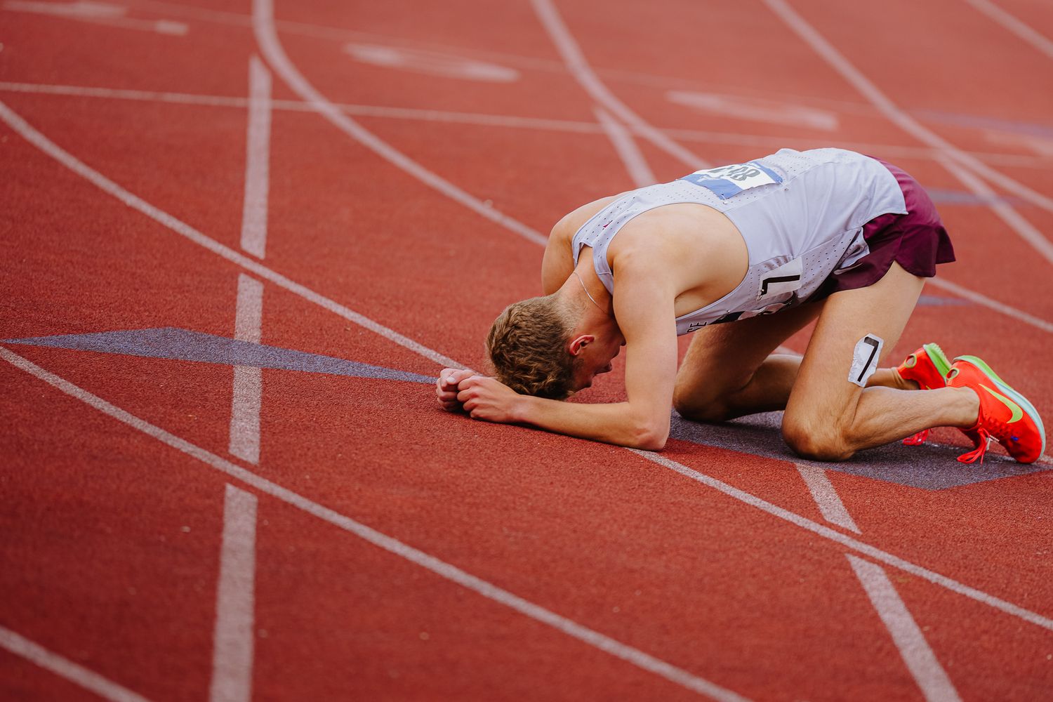 Runner lies exhausted on red track surface after race completion.