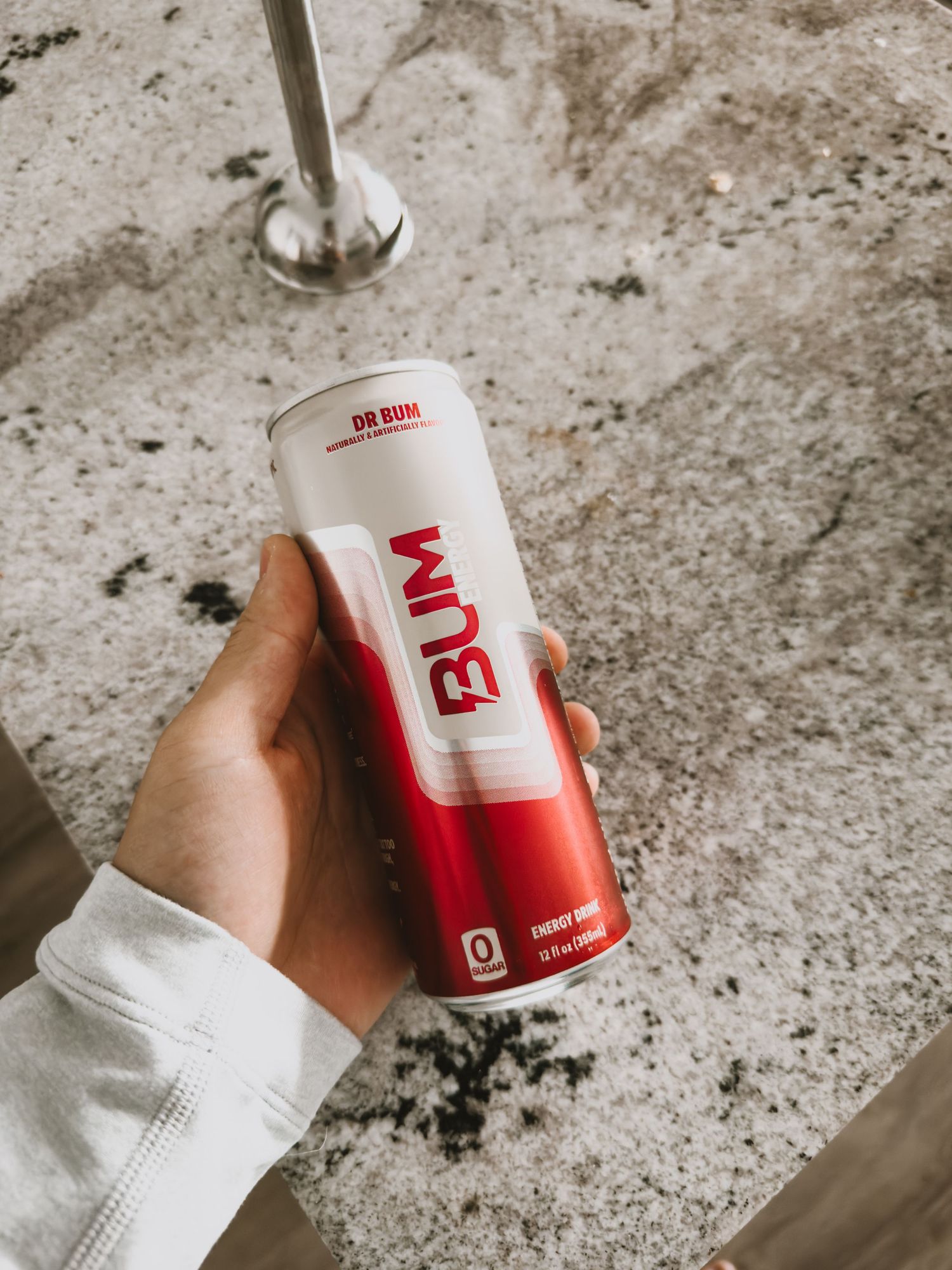 Hand holding a red and white Bang energy drink can against a textured concrete background.