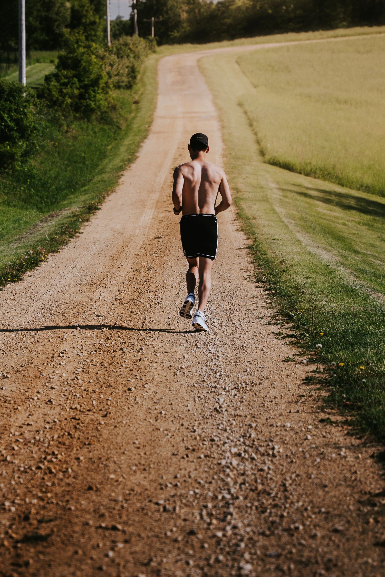 A figure jogs along a winding dirt path through golden fields on a sunny summer day.