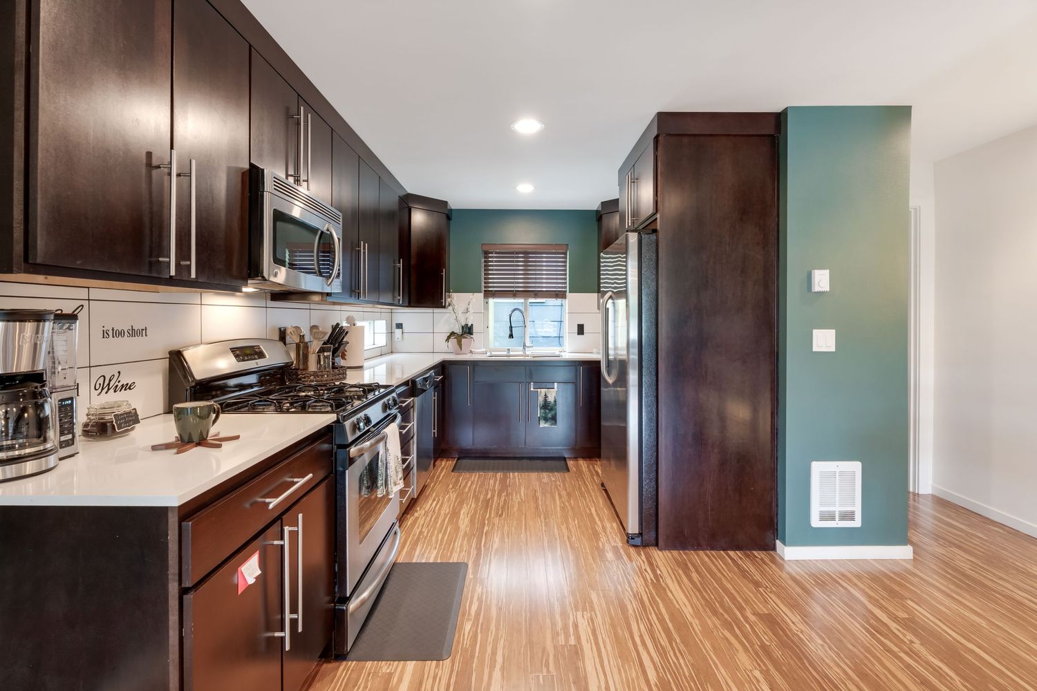 Modern kitchen with dark wood cabinets, stainless steel appliances, white countertops, teal accent wall, and hardwood floors.