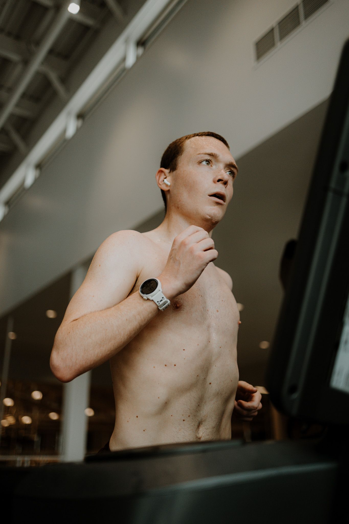 Artistic portrait of a shirtless person wearing a watch looking upward in moody lighting against an industrial backdrop.