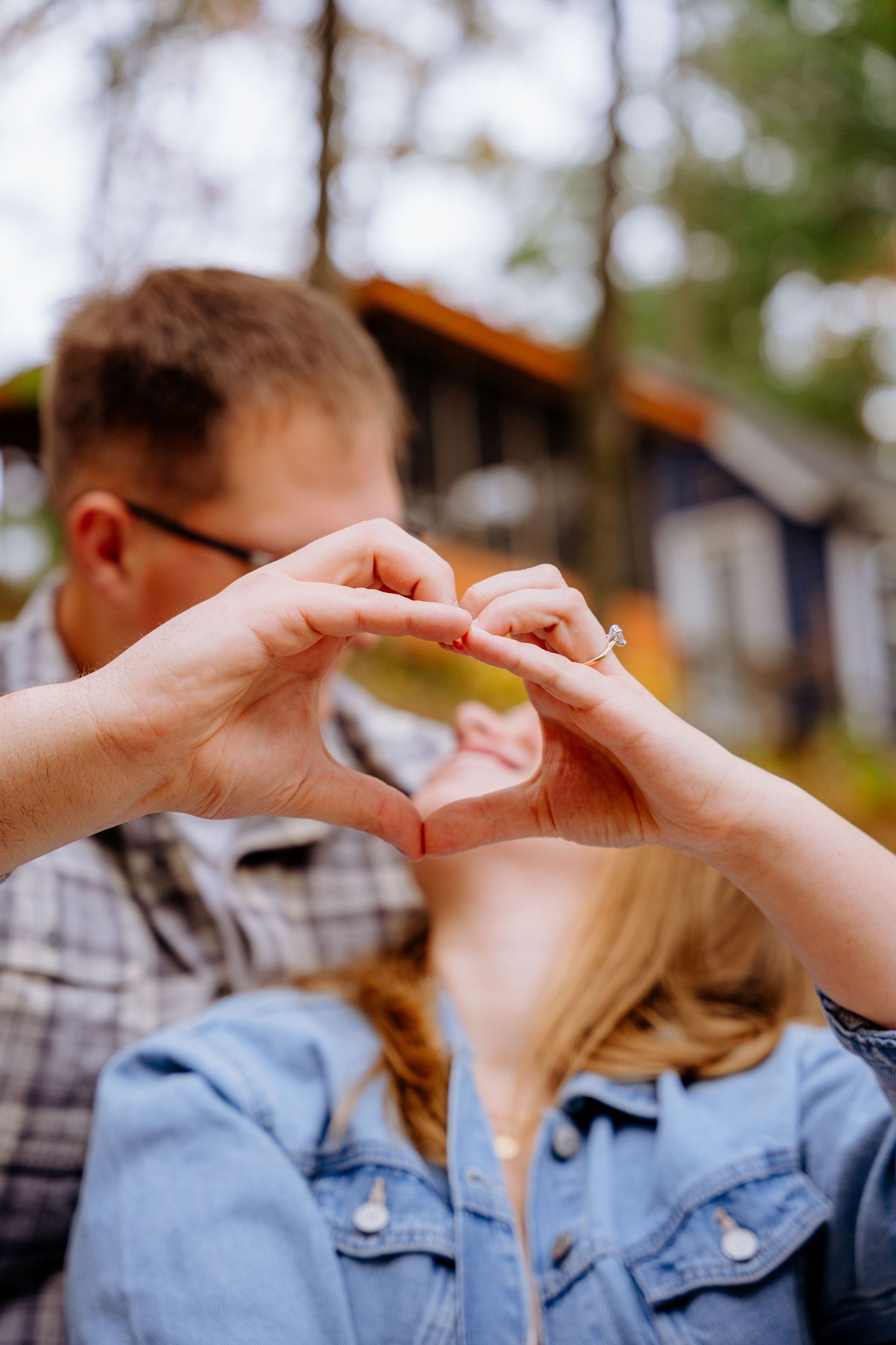 Two people making a heart shape with their hands against a blurred outdoor background.