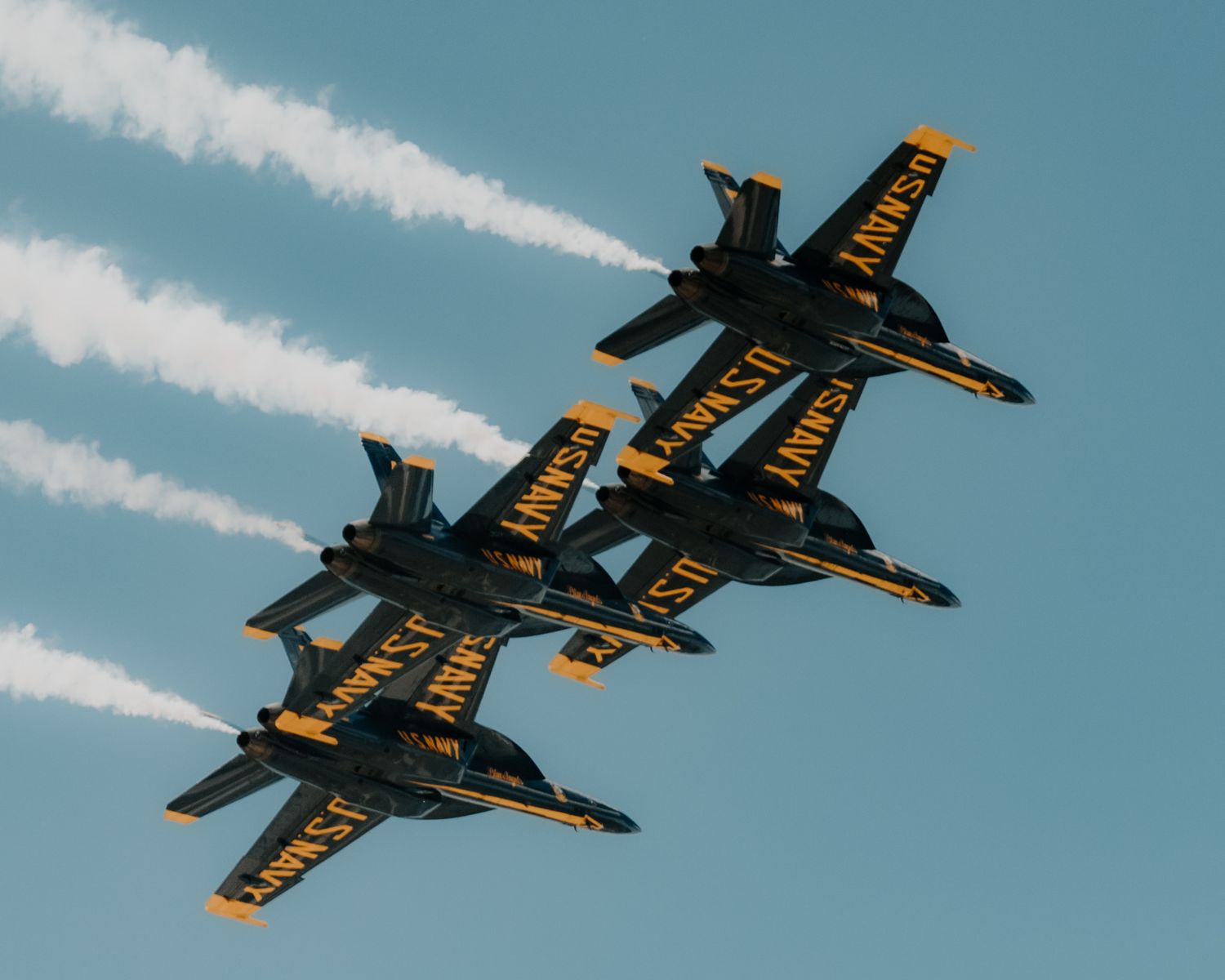 Blue Angels F/A-18 Hornet jets perform aerial maneuvers with white contrails against blue sky.