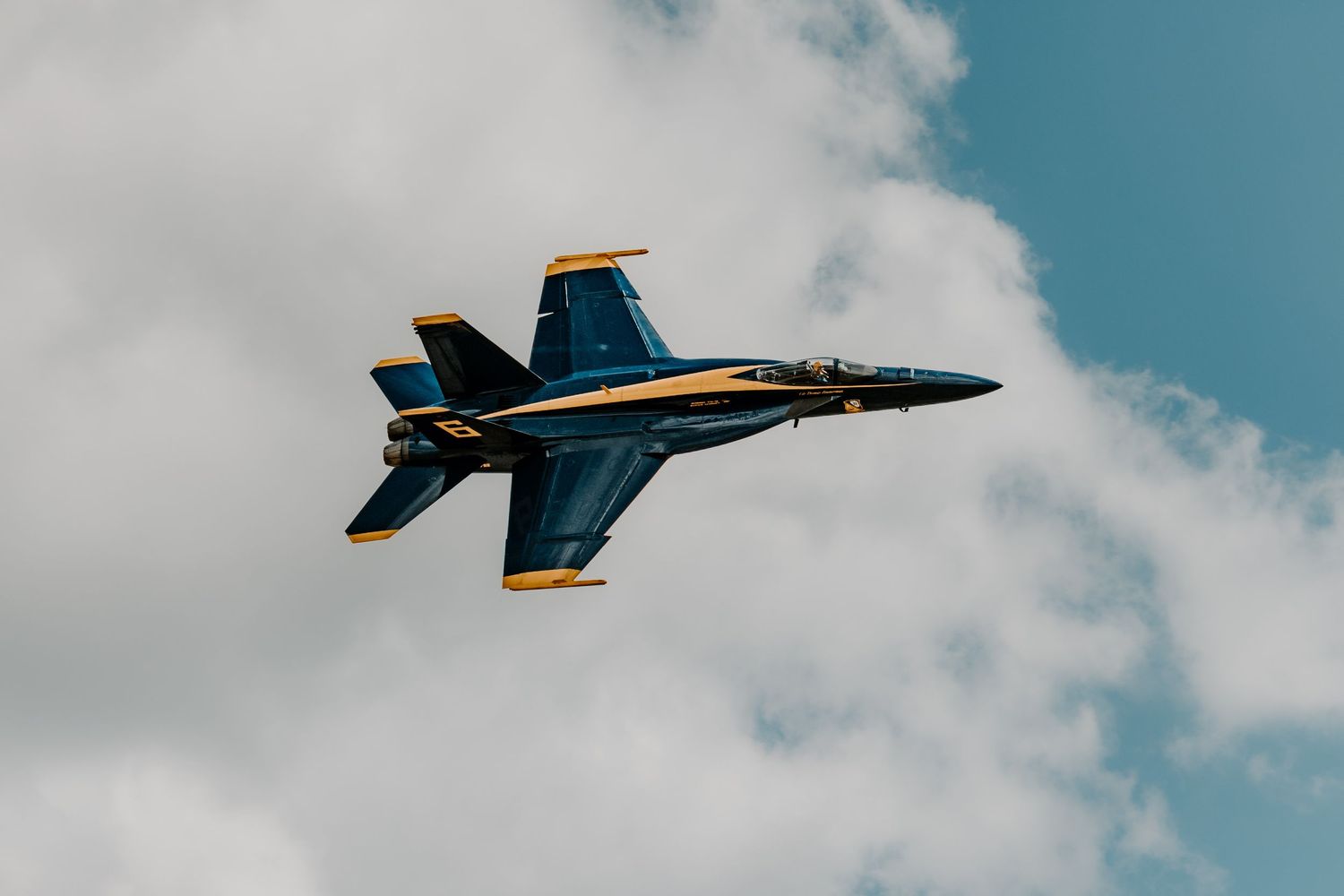 A U.S. Navy Blue Angels F/A-18 Hornet performs aerial maneuvers against a cloudy blue sky during an airshow.