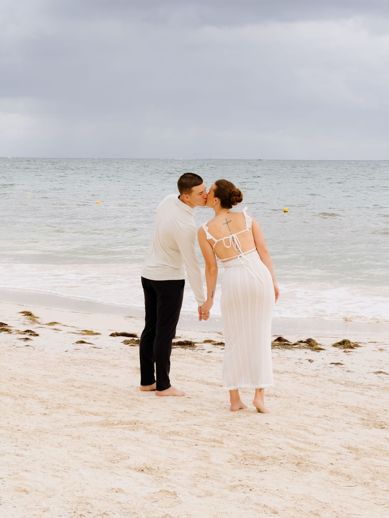 A romantic beach scene with a couple in white and black attire walking along the sandy shoreline.