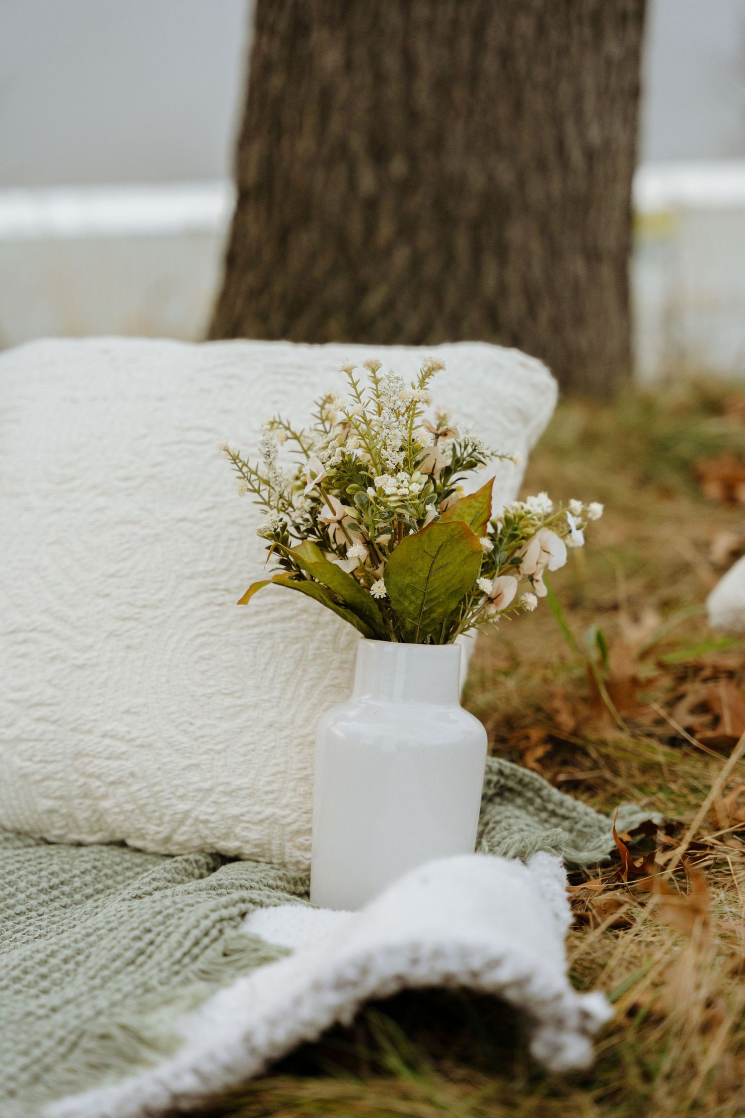 A white ceramic vase with delicate flowers sits beside a cozy white towel on a textured green surface.