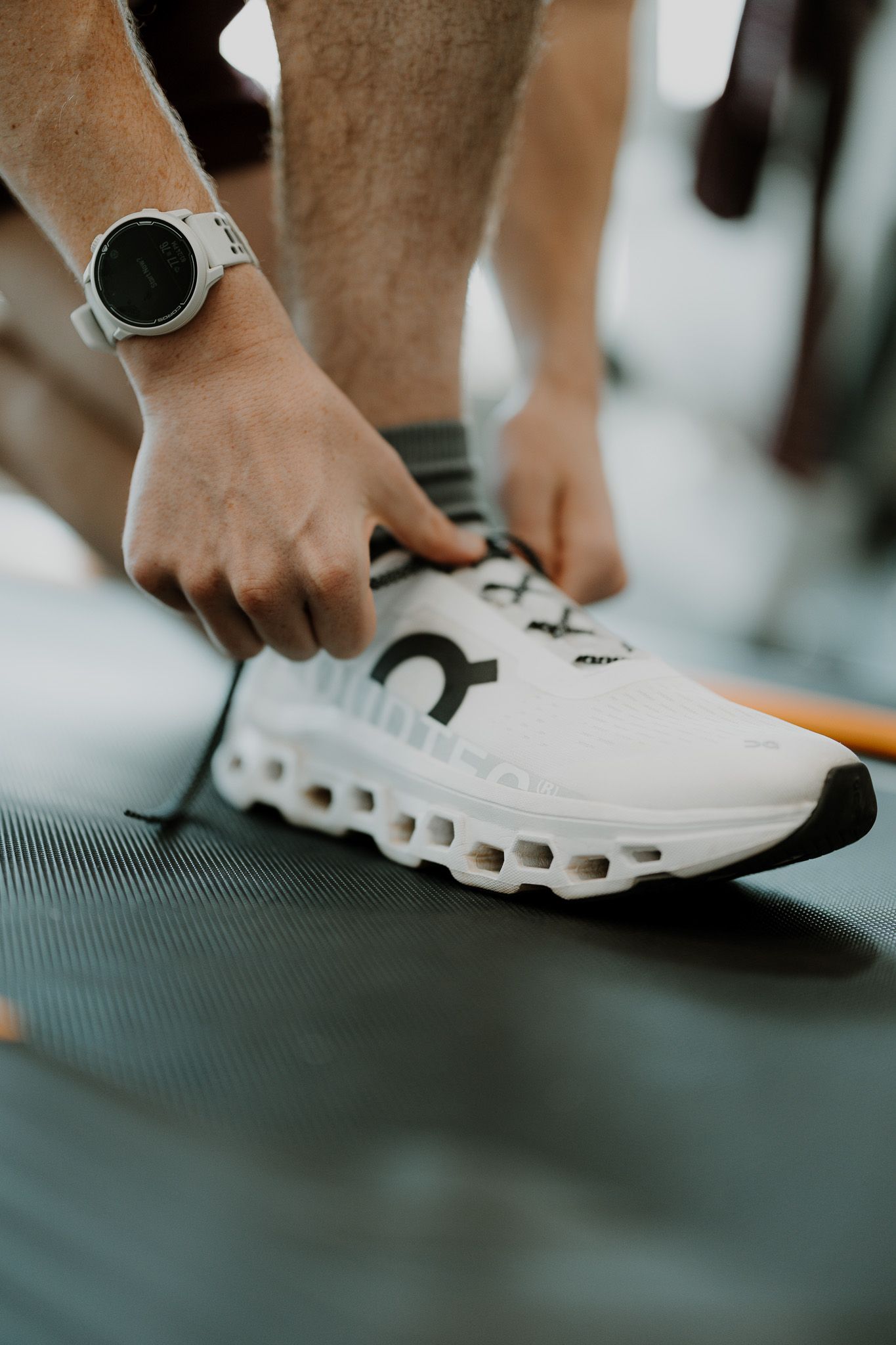 Close-up view of hands adjusting white athletic shoes on a dark exercise mat.