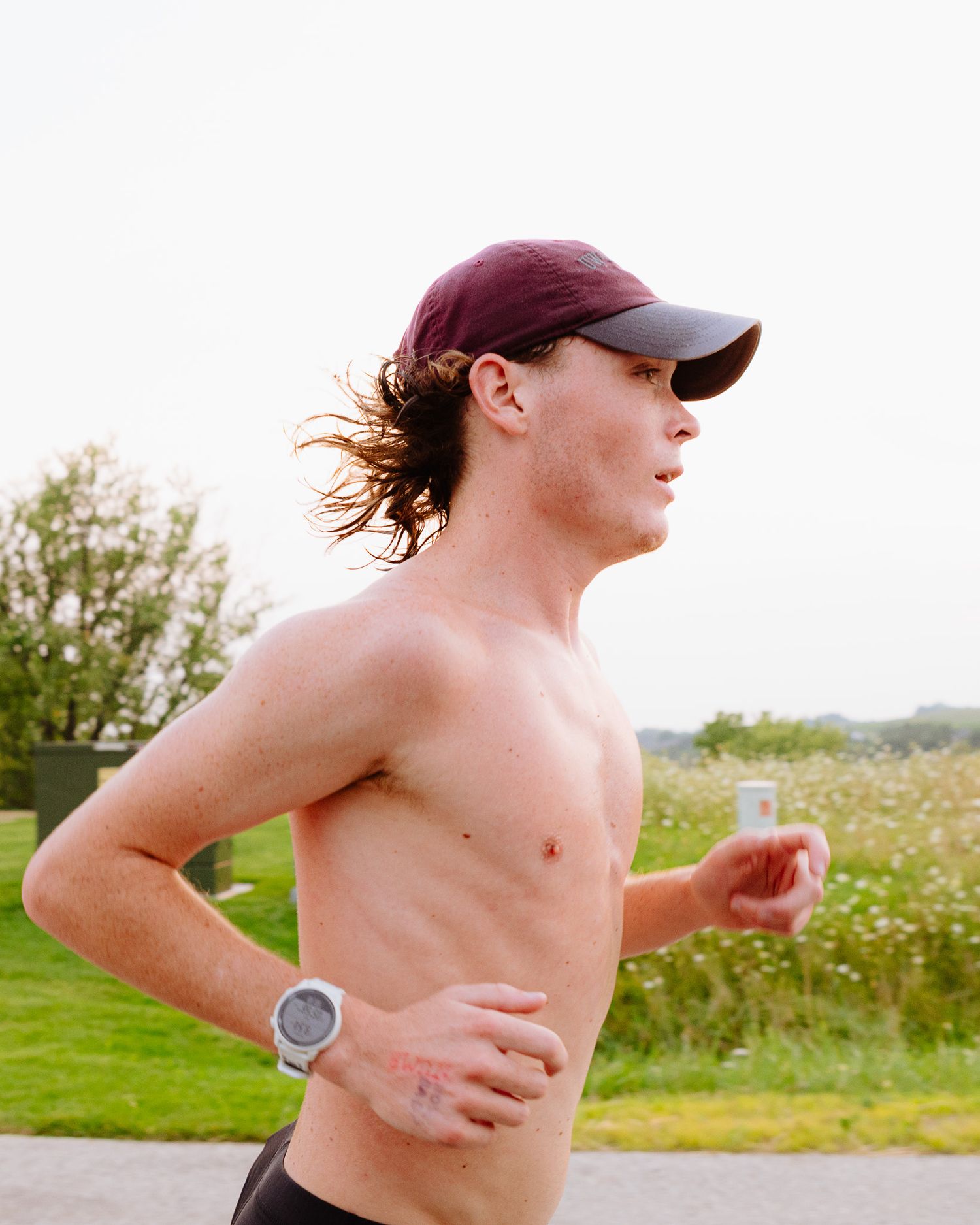 Runner in athletic gear jogging through a grassy field on a sunny day.