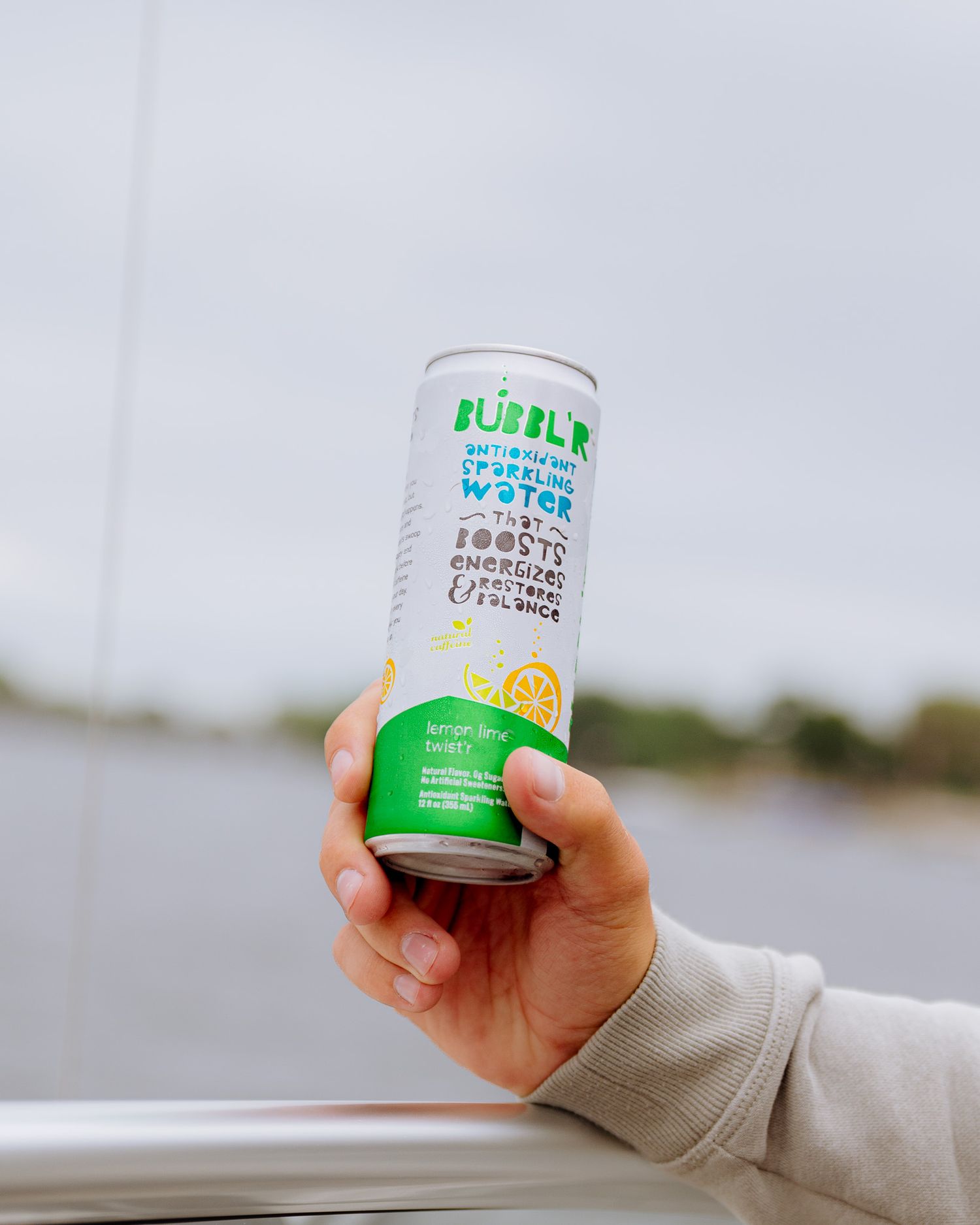 Hand holding a green and white bubble tea can against a blurry background.