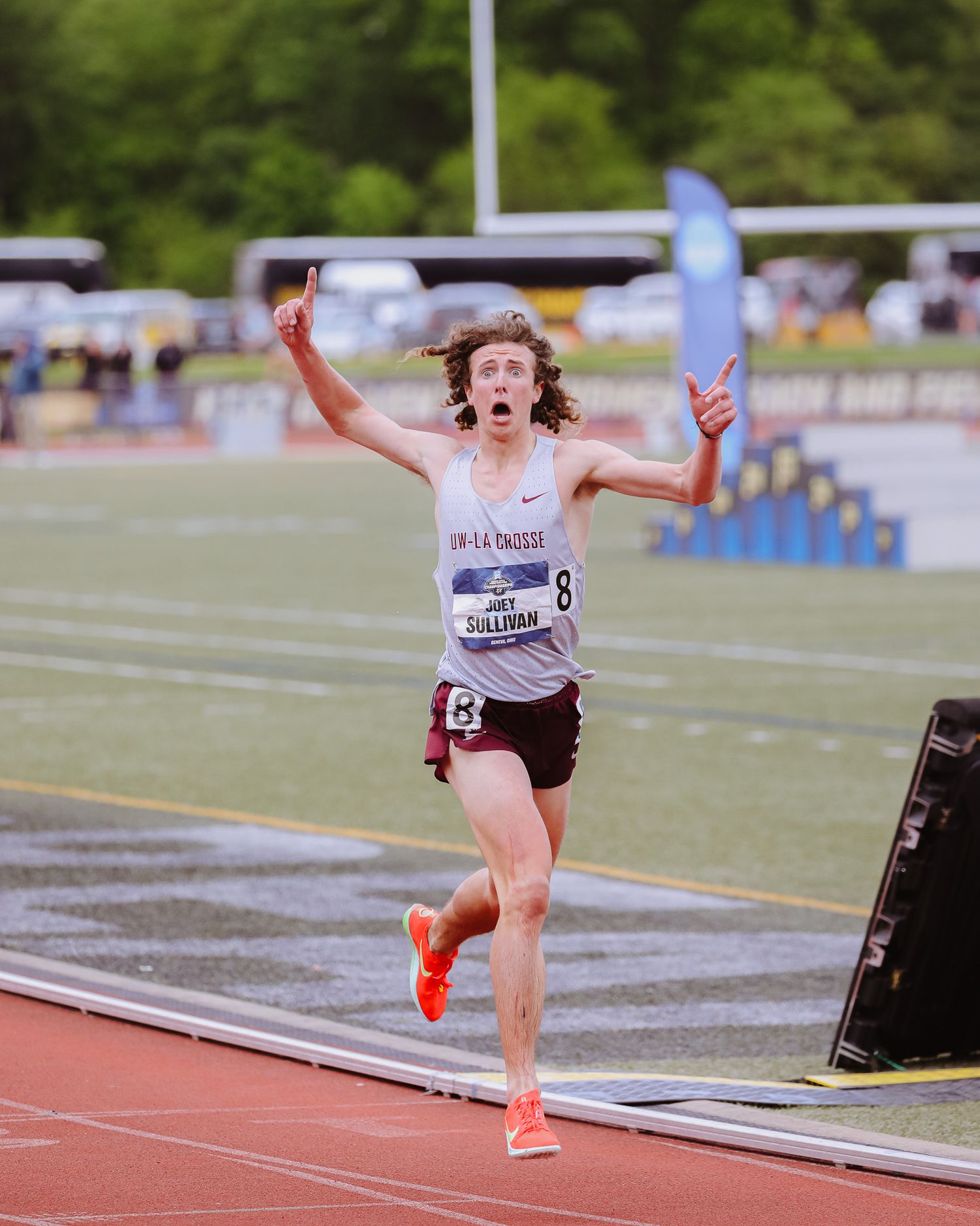 Runner celebrates with arms raised while crossing finish line at track meet competition.