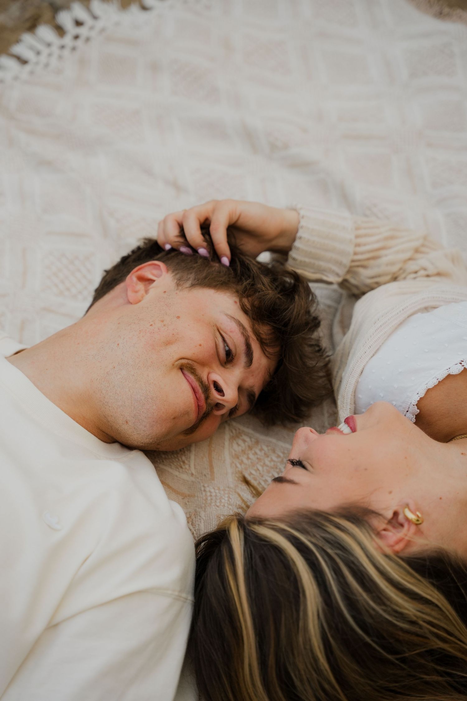 Two people lying close together on white bedding in an intimate moment.