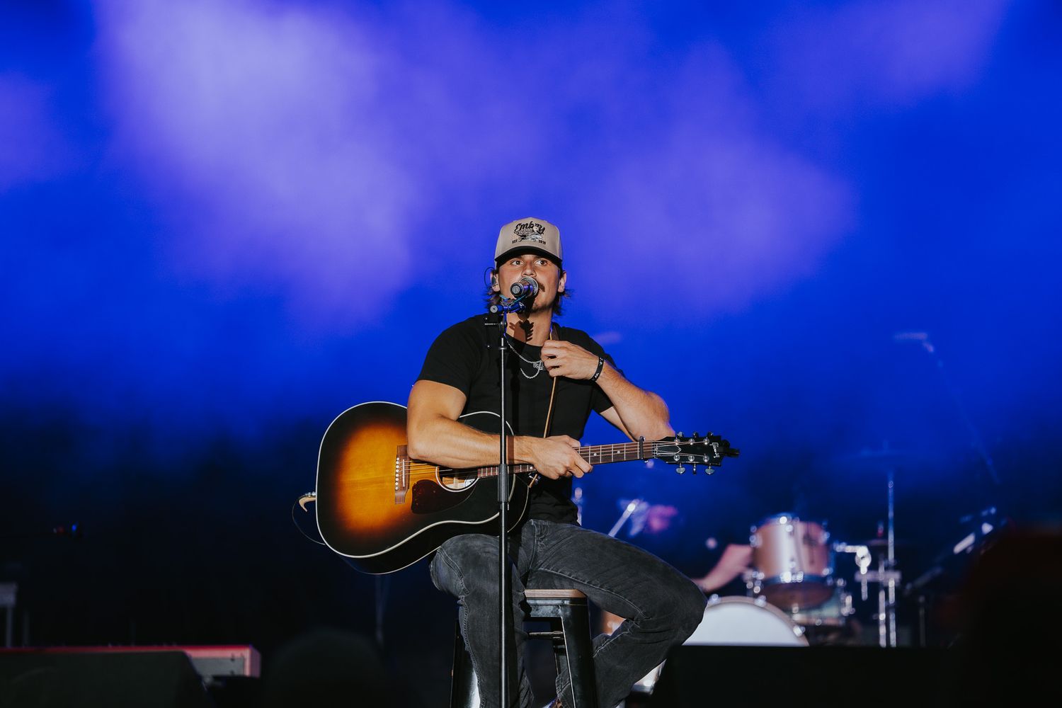Concert performer silhouetted against blue stage lighting while playing acoustic guitar.