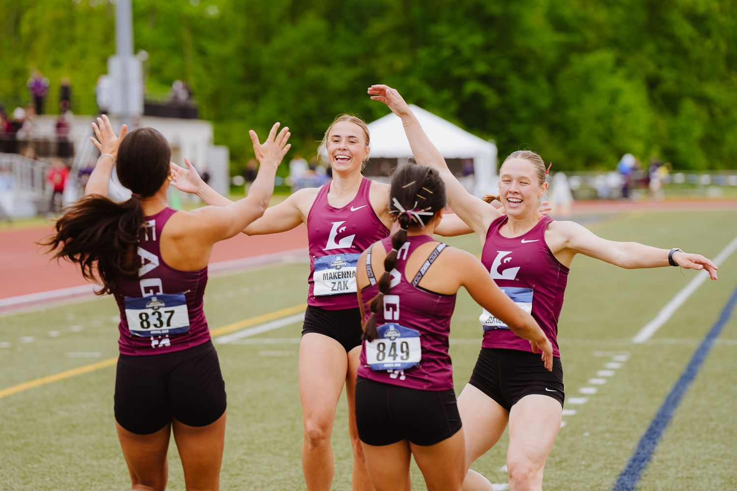 Female athletes in maroon uniforms celebrating together on a track field.