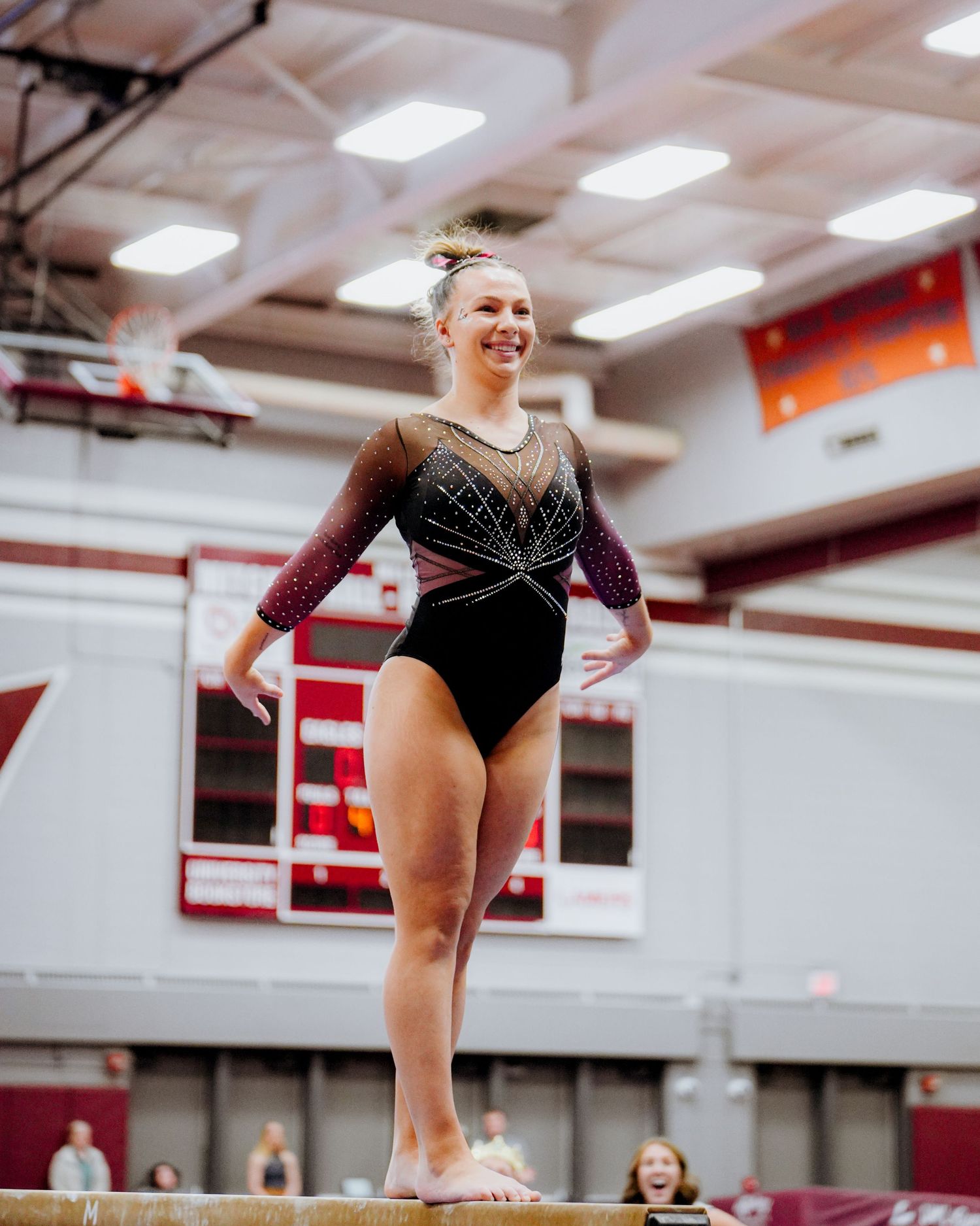 A gymnast performs a precise balancing routine on the beam during a competitive event in a gymnasium.