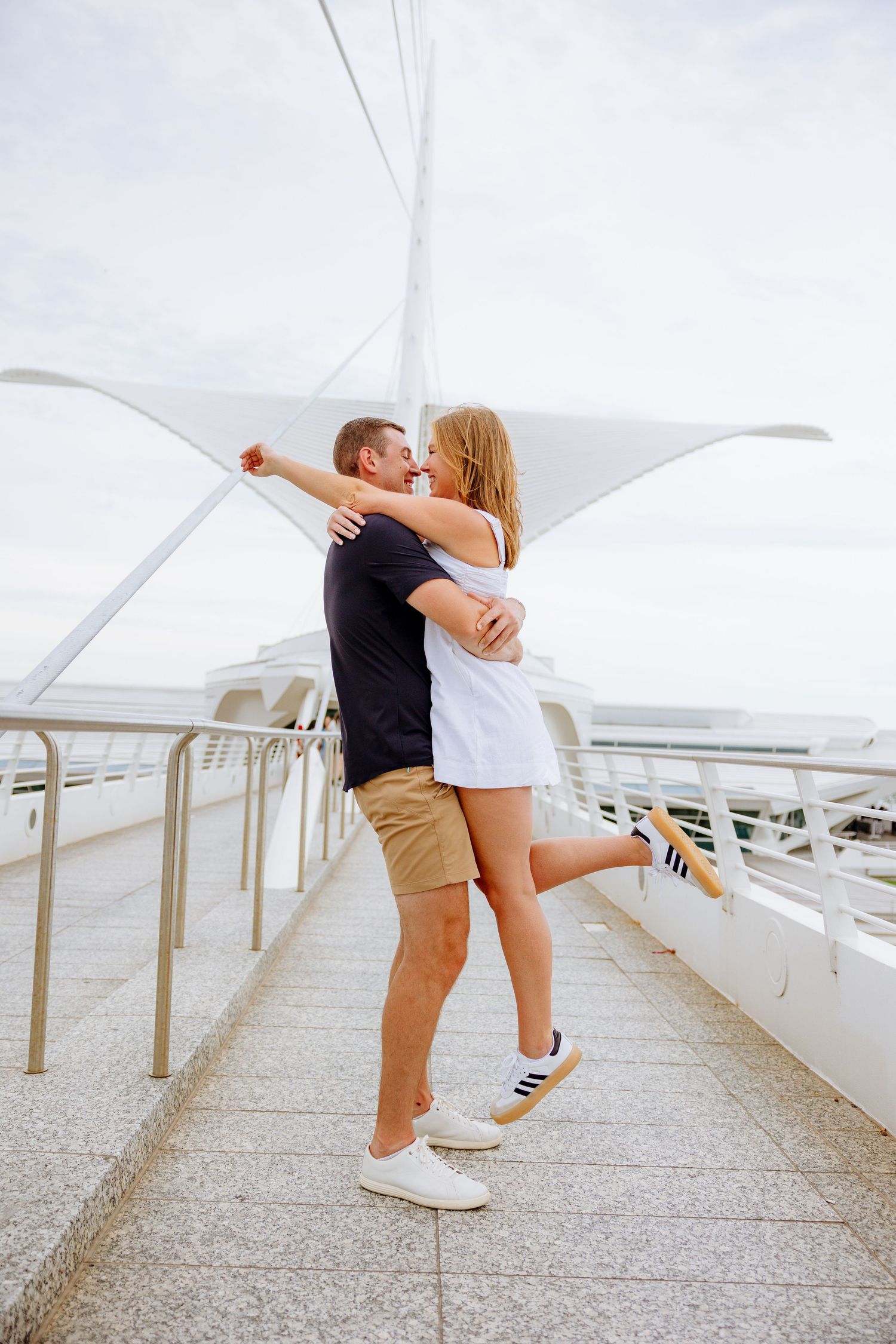 A couple shares a romantic moment under billowing white fabric in an outdoor setting with modern architecture.