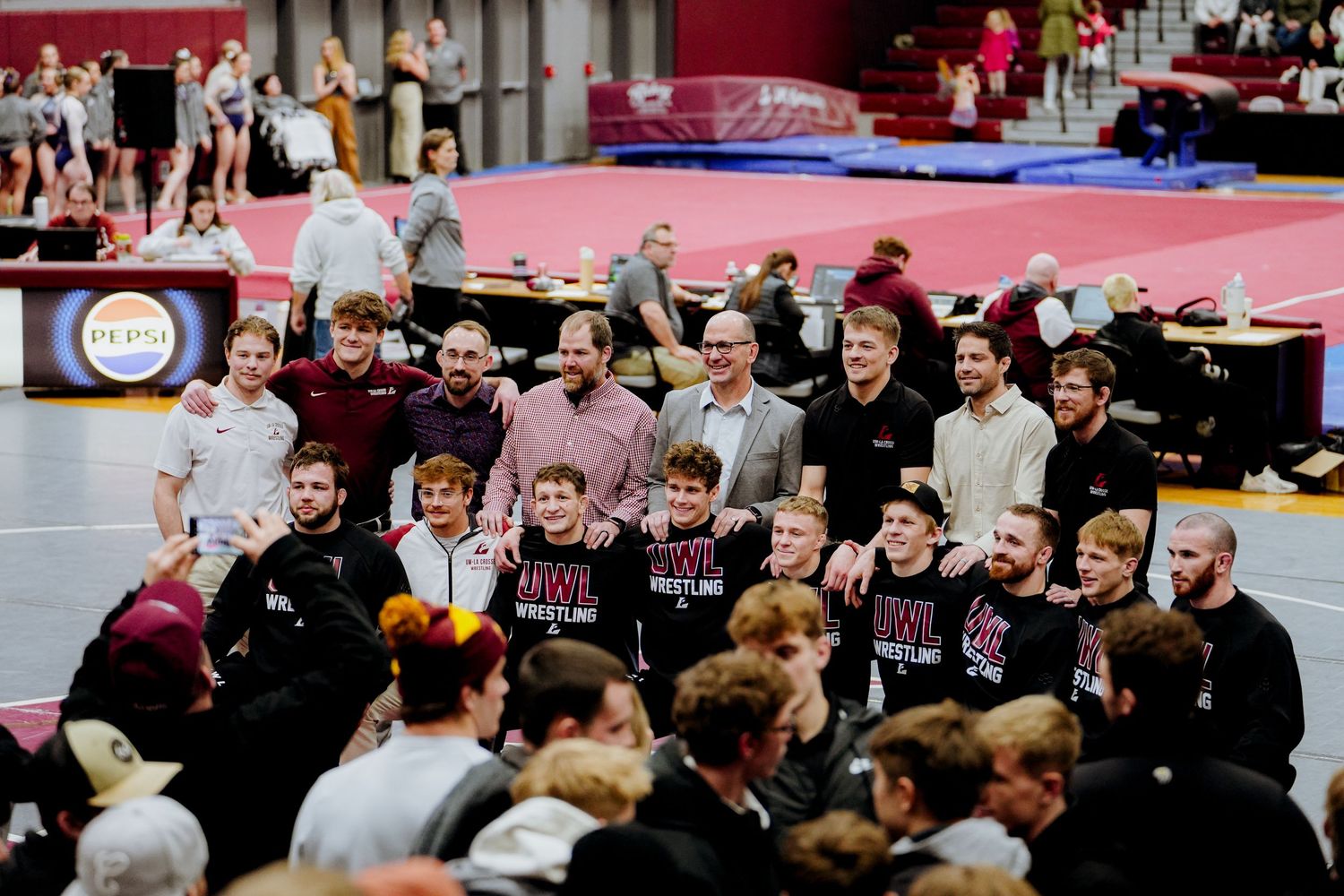 Martial arts competitors and spectators gather around red and blue mats during a tournament event.