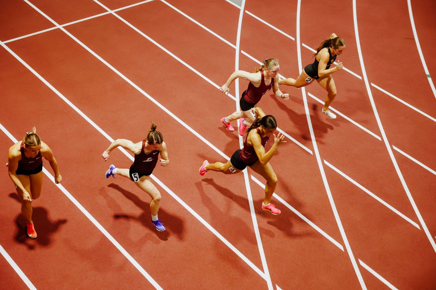 Aerial view of athletes competing in track race on red running surface with white lane lines.